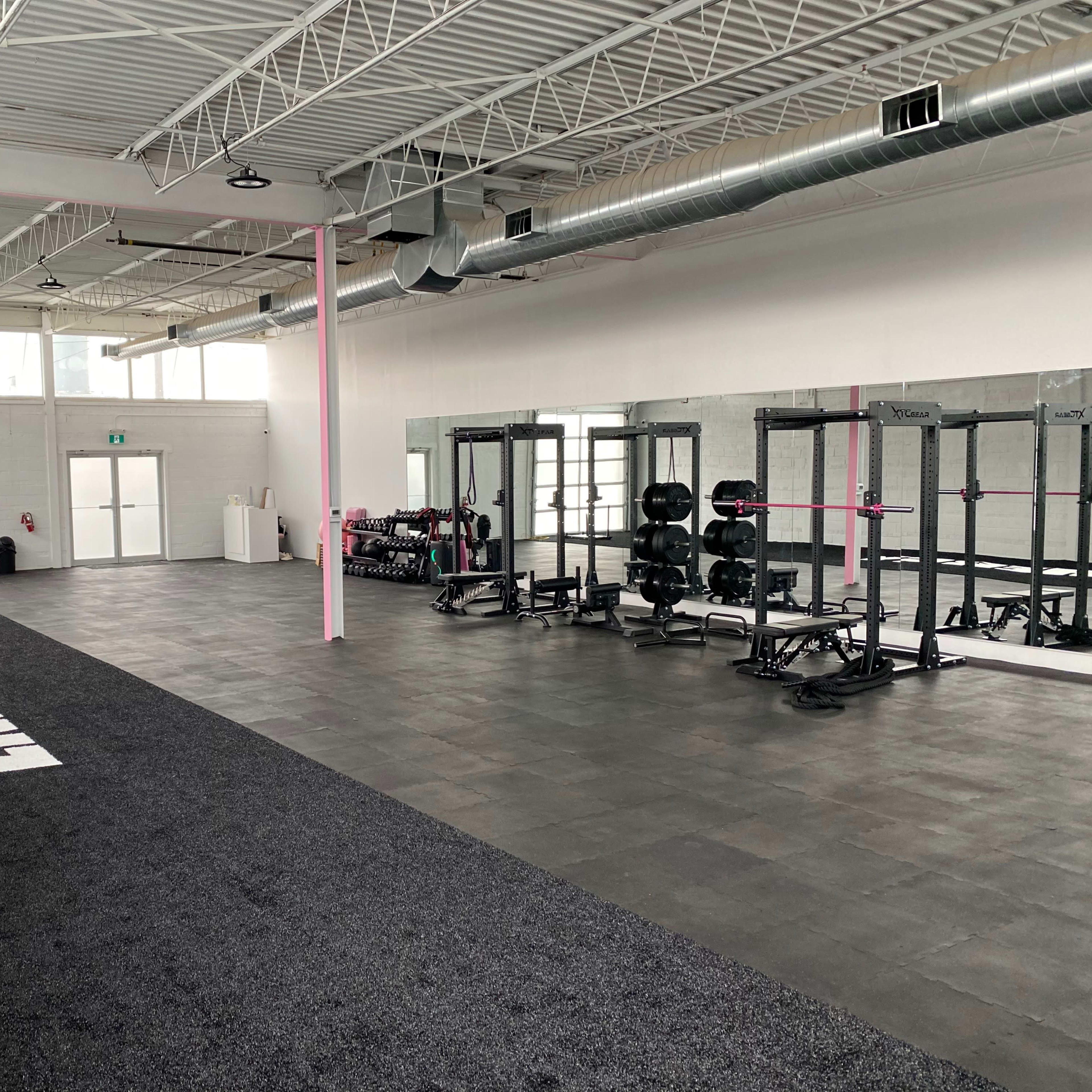 A spacious gym interior featuring black rubber flooring, weightlifting equipment, and large mirrors along one wall.