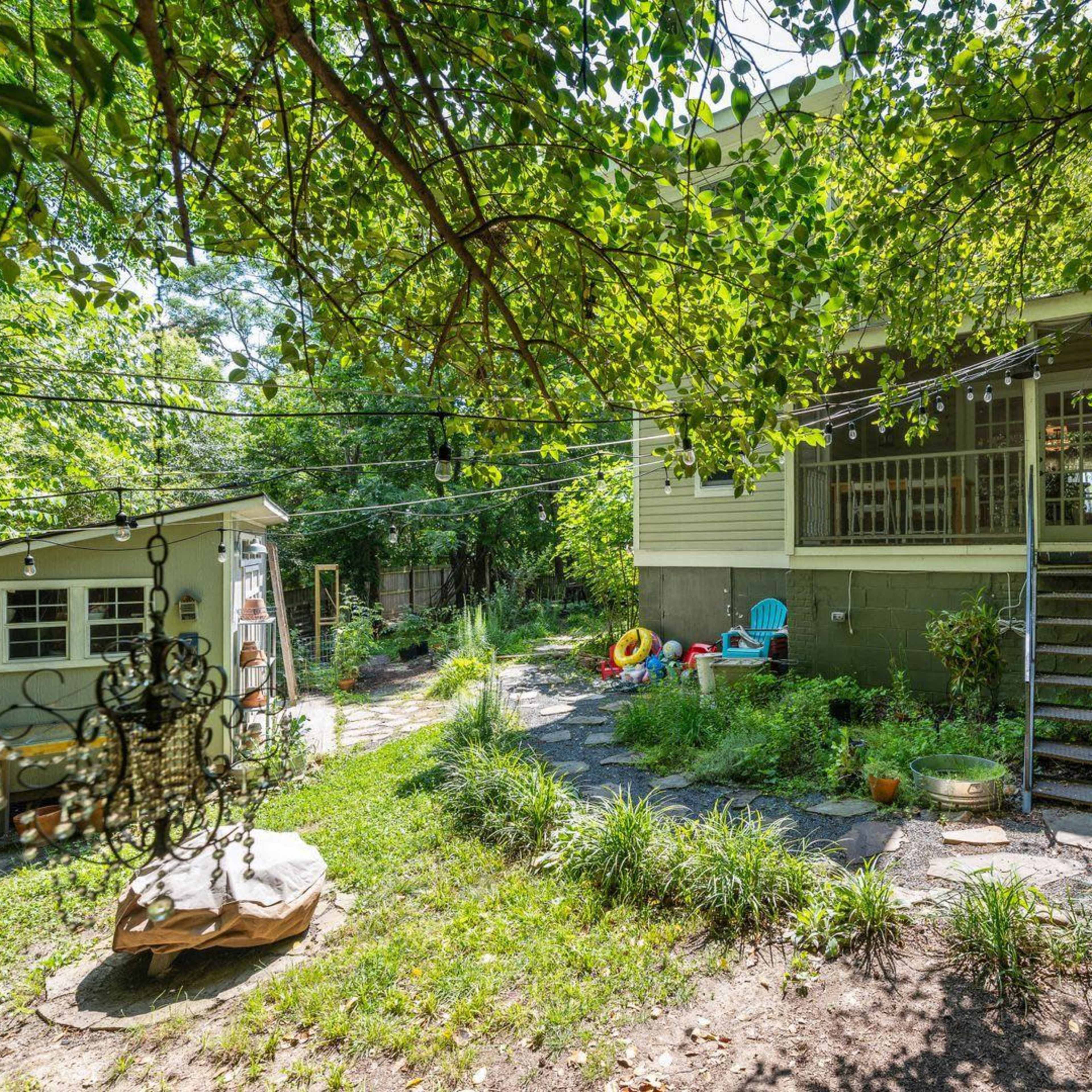 A backyard with a well-maintained garden, a small shed, and a multi-level house surrounded by trees.