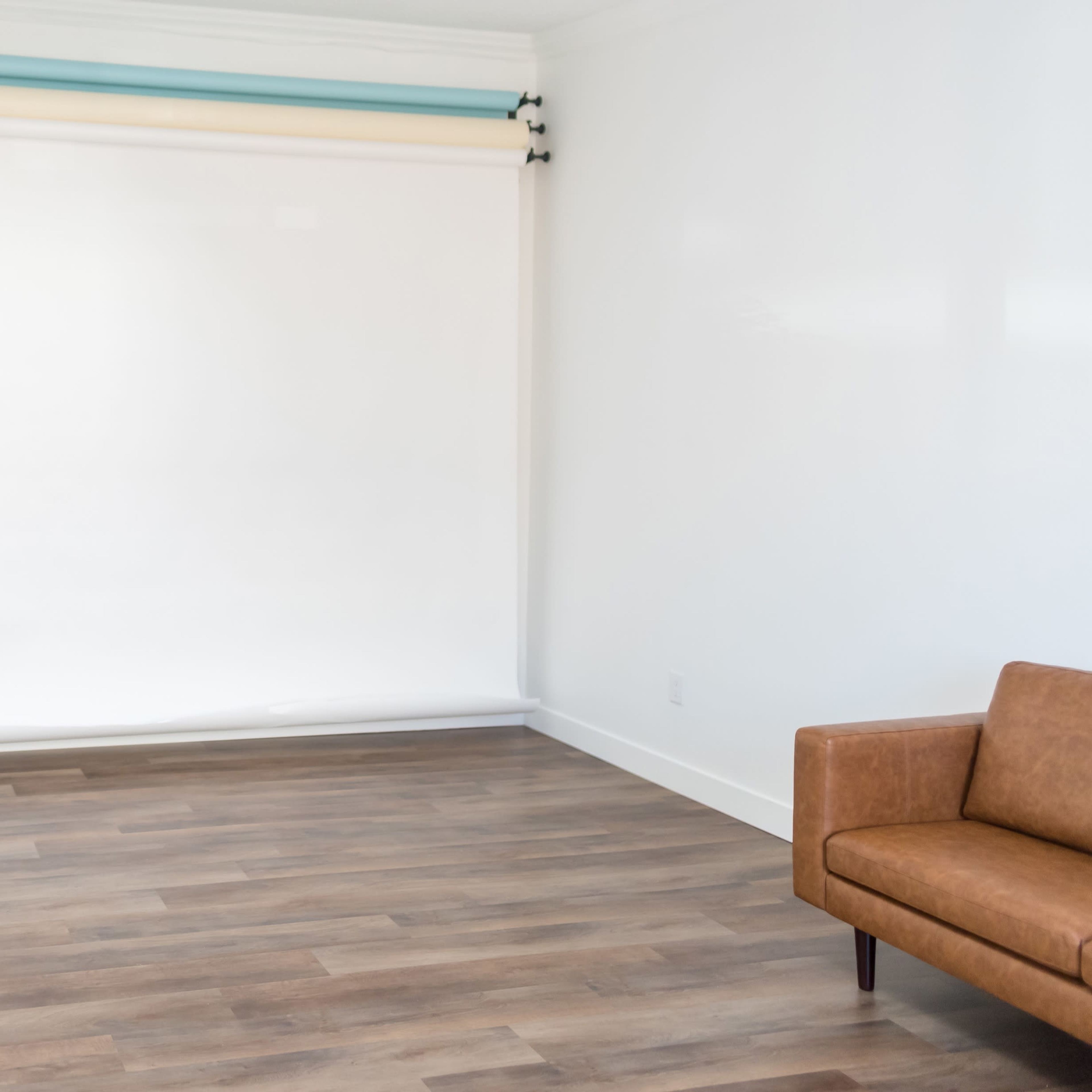 A spacious interior room with hardwood floors, a closed door, and a white backdrop mounted on a roller system against a plain wall.