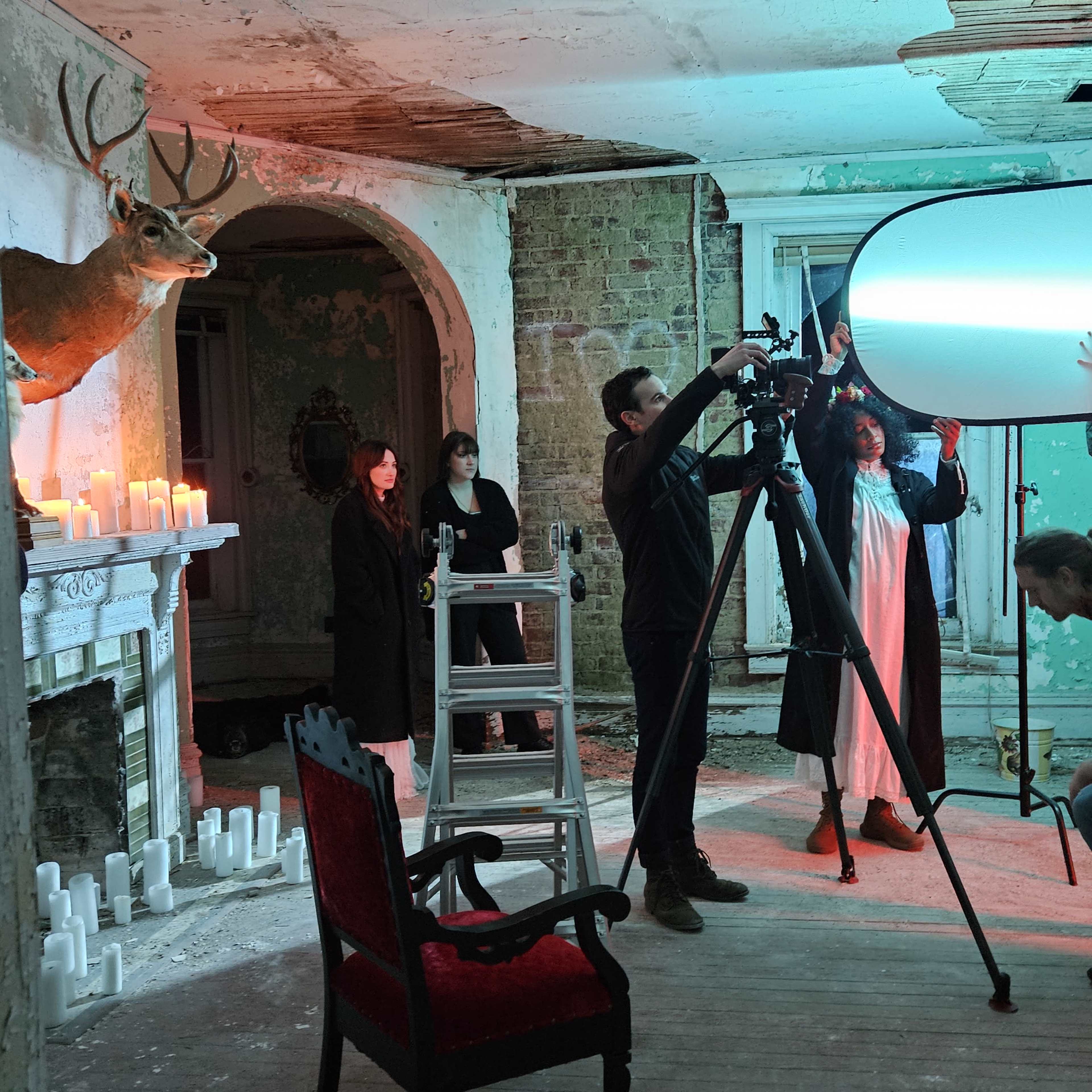 A film crew sets up equipment in an abandoned room decorated with deer mounts and candles.