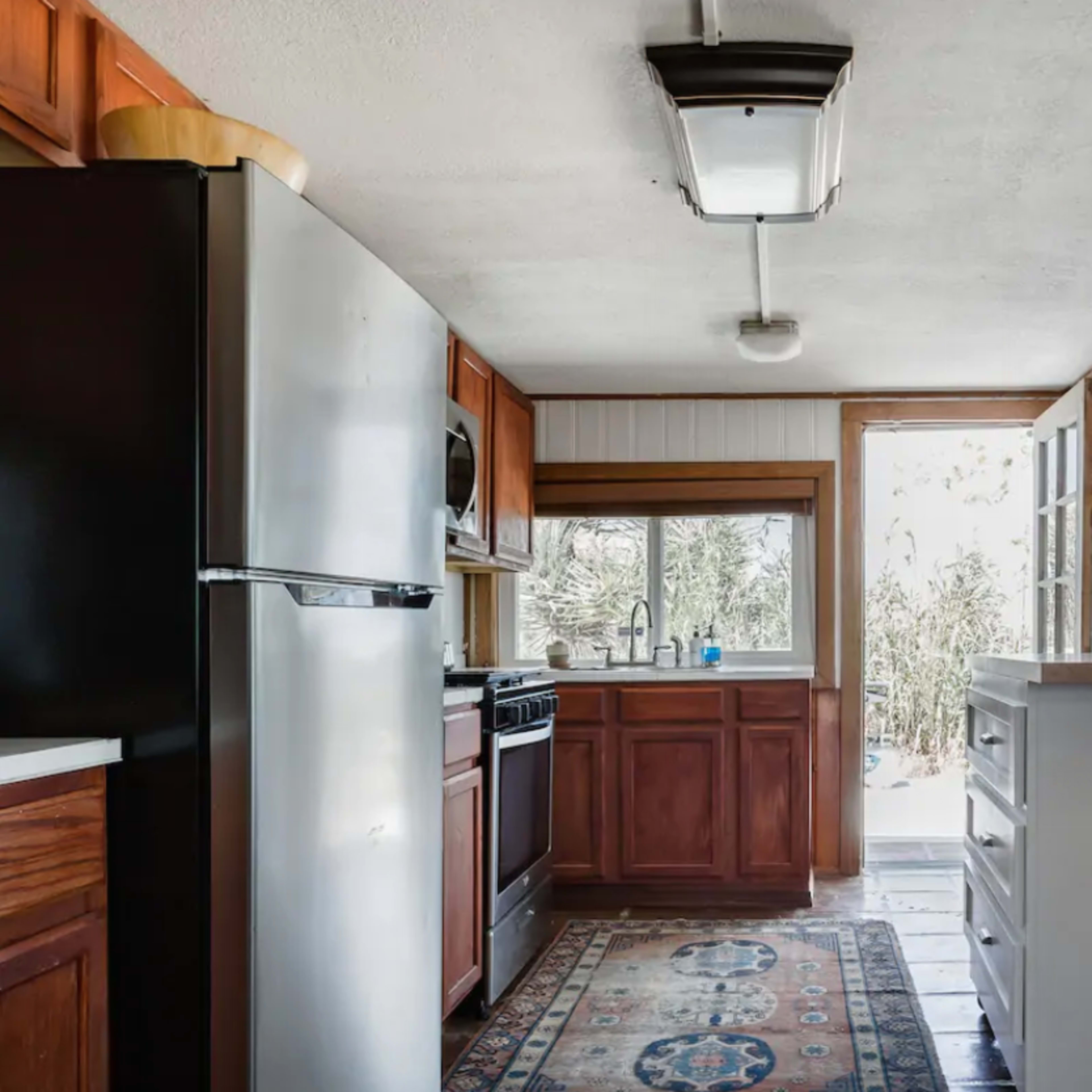 A kitchen with stainless steel appliances, wooden cabinets, and large windows allowing natural light to enter.