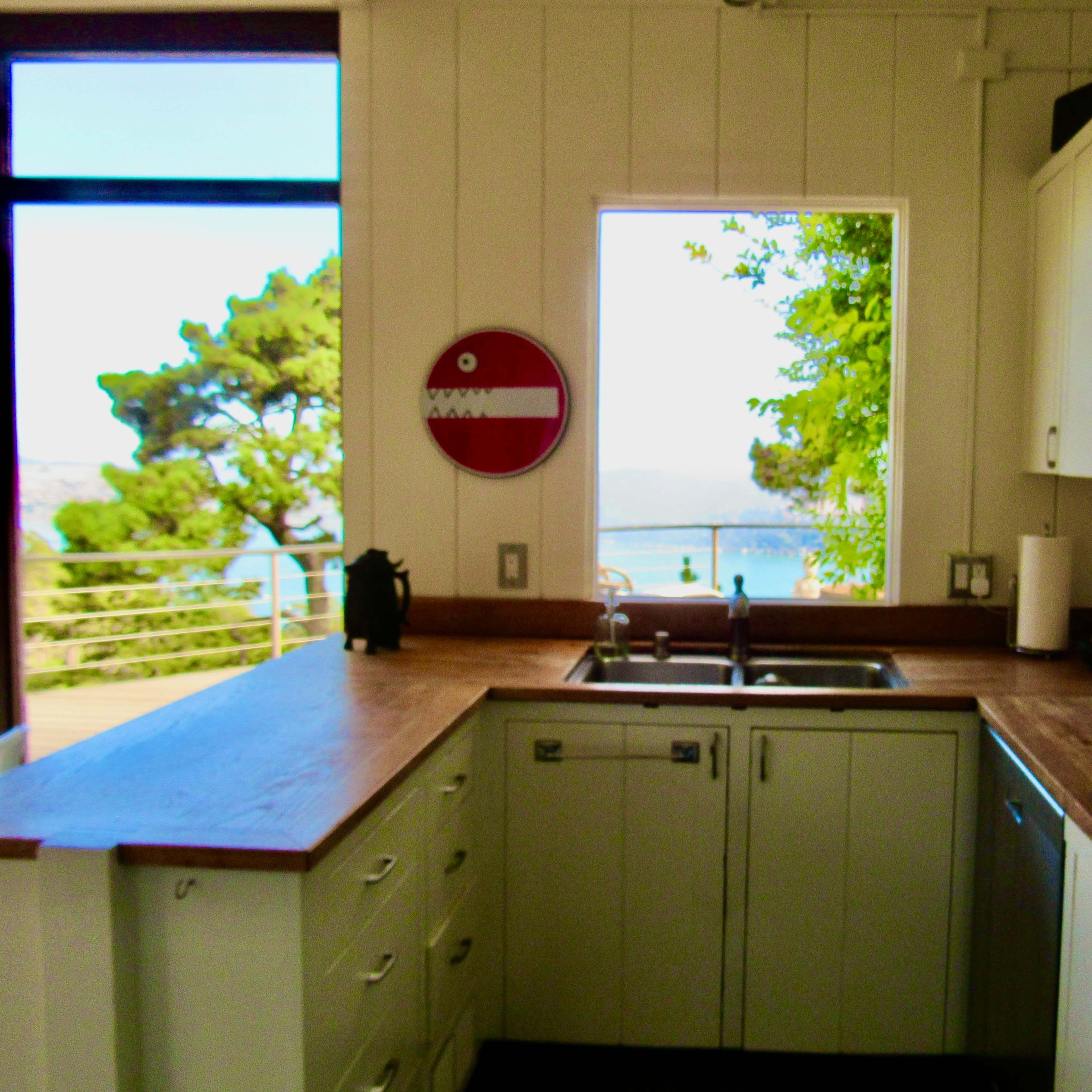 A modern kitchen features white cabinets, wooden countertops, and a large window with a scenic view of the outside.