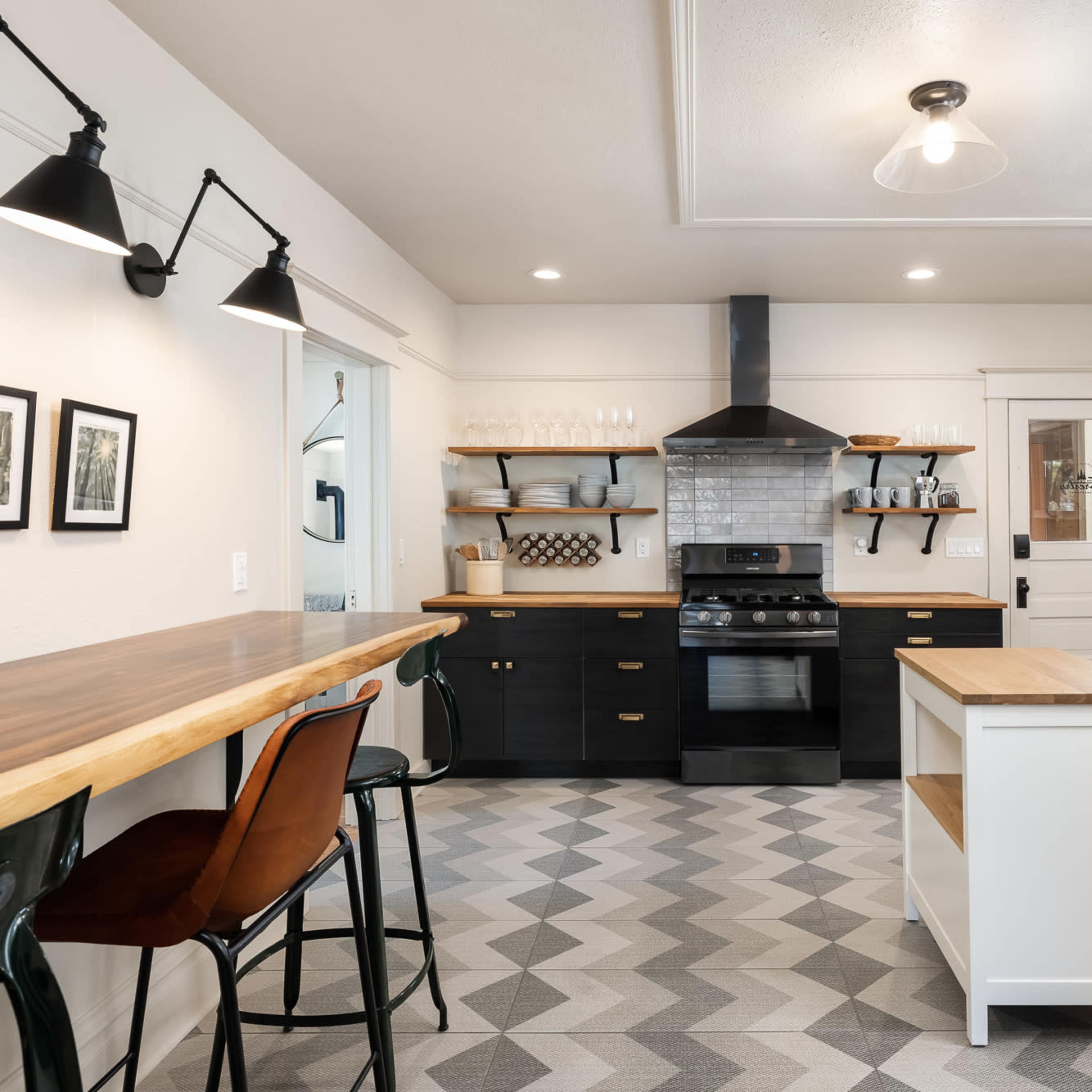 A modern kitchen features black cabinets, wooden counters, a stainless steel stove, and patterned tile flooring.