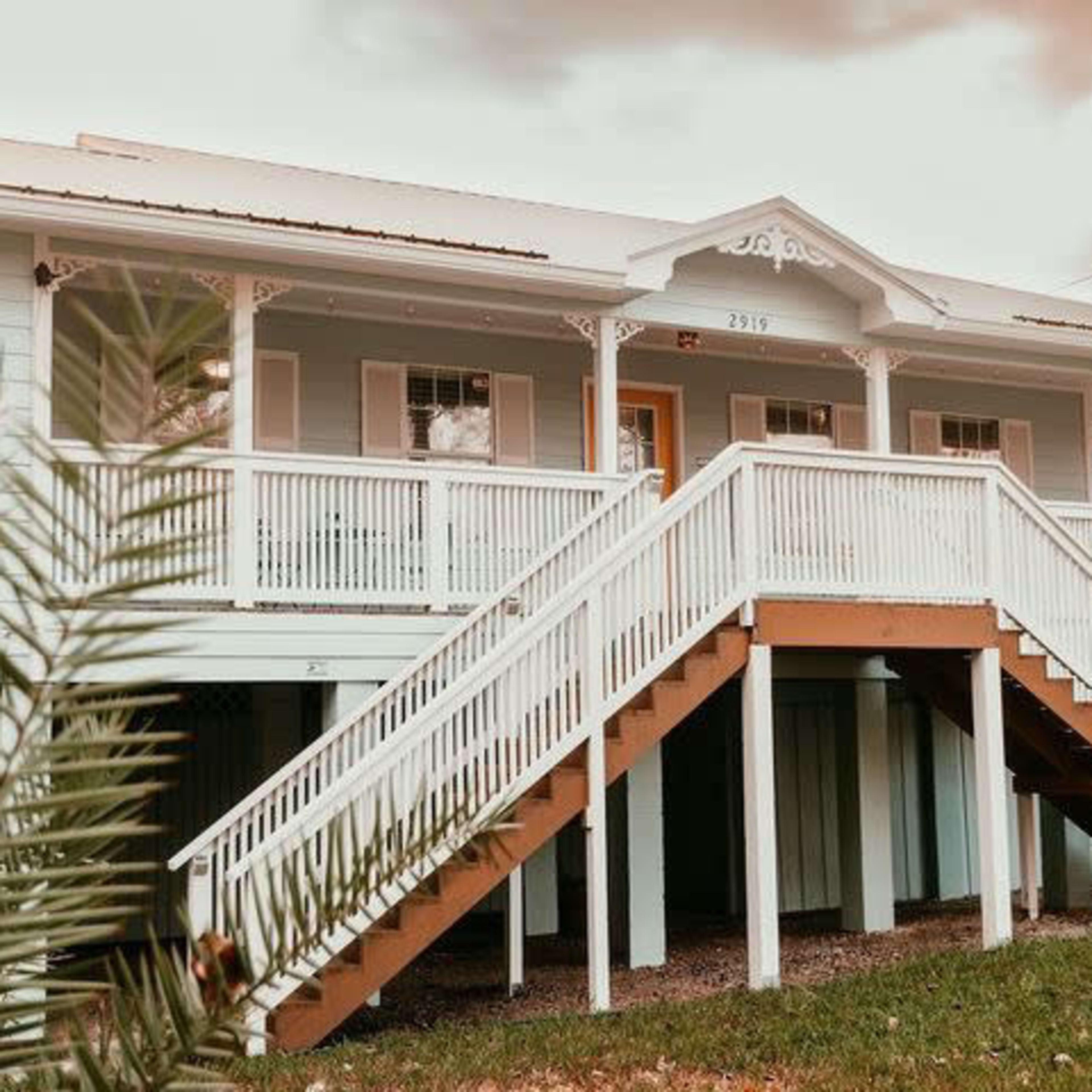 A two-story house with a light blue exterior and a white wooden staircase leading to the entrance.