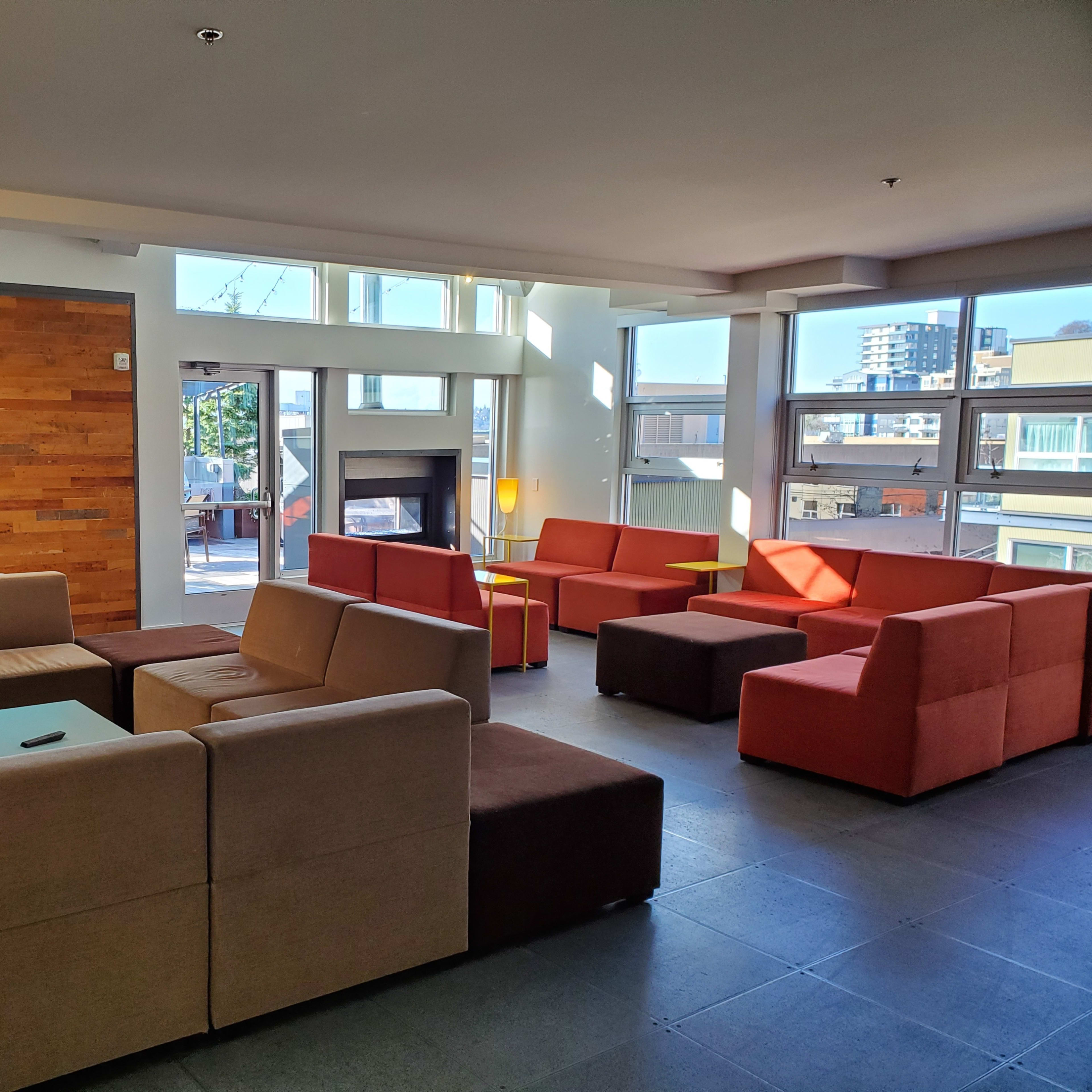 A modern lounge area featuring several sofa arrangements in neutral and warm colors, illuminated by natural light from large windows.