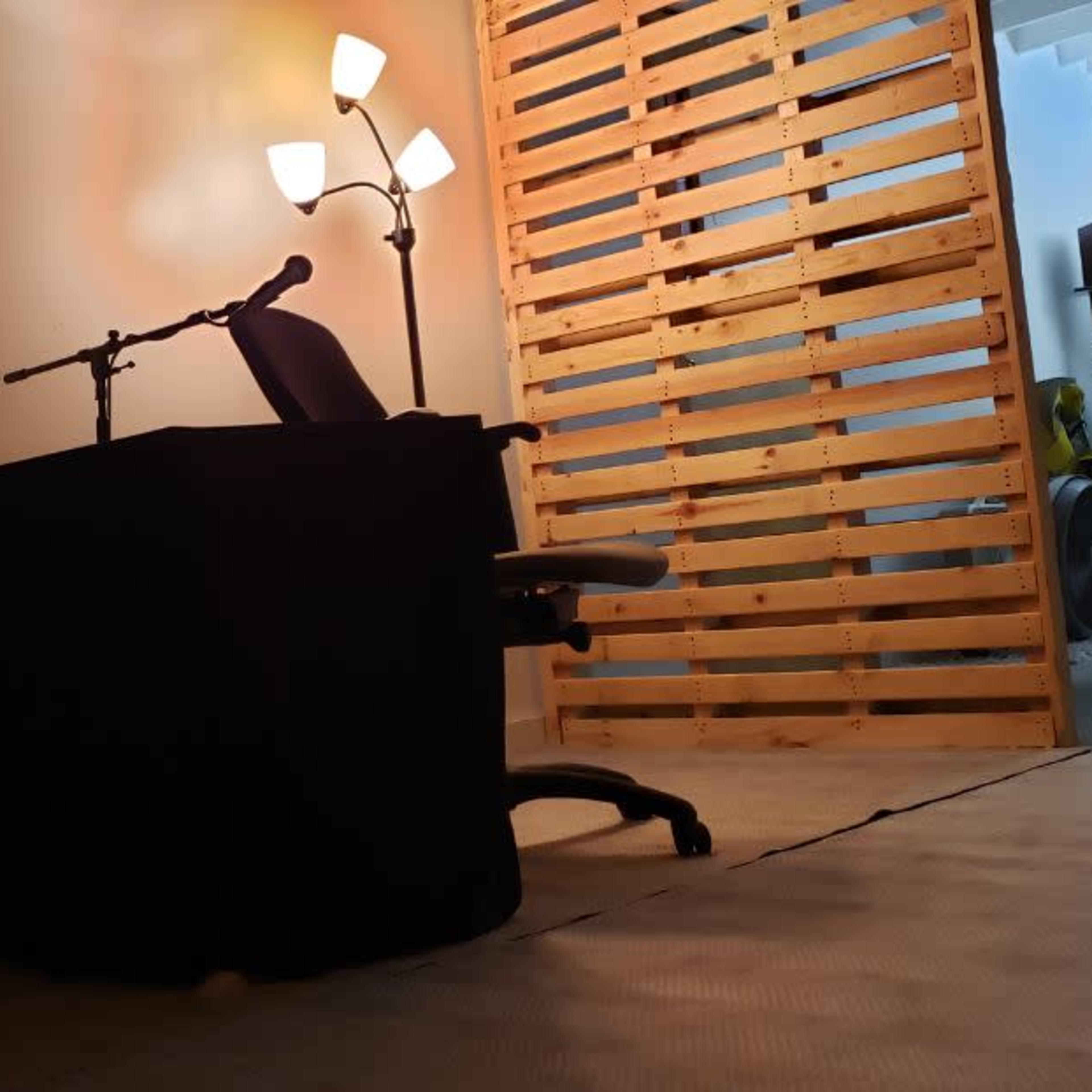 A simple workspace with two office chairs facing a small, dark table illuminated by a floor lamp, set against a wooden slatted wall.