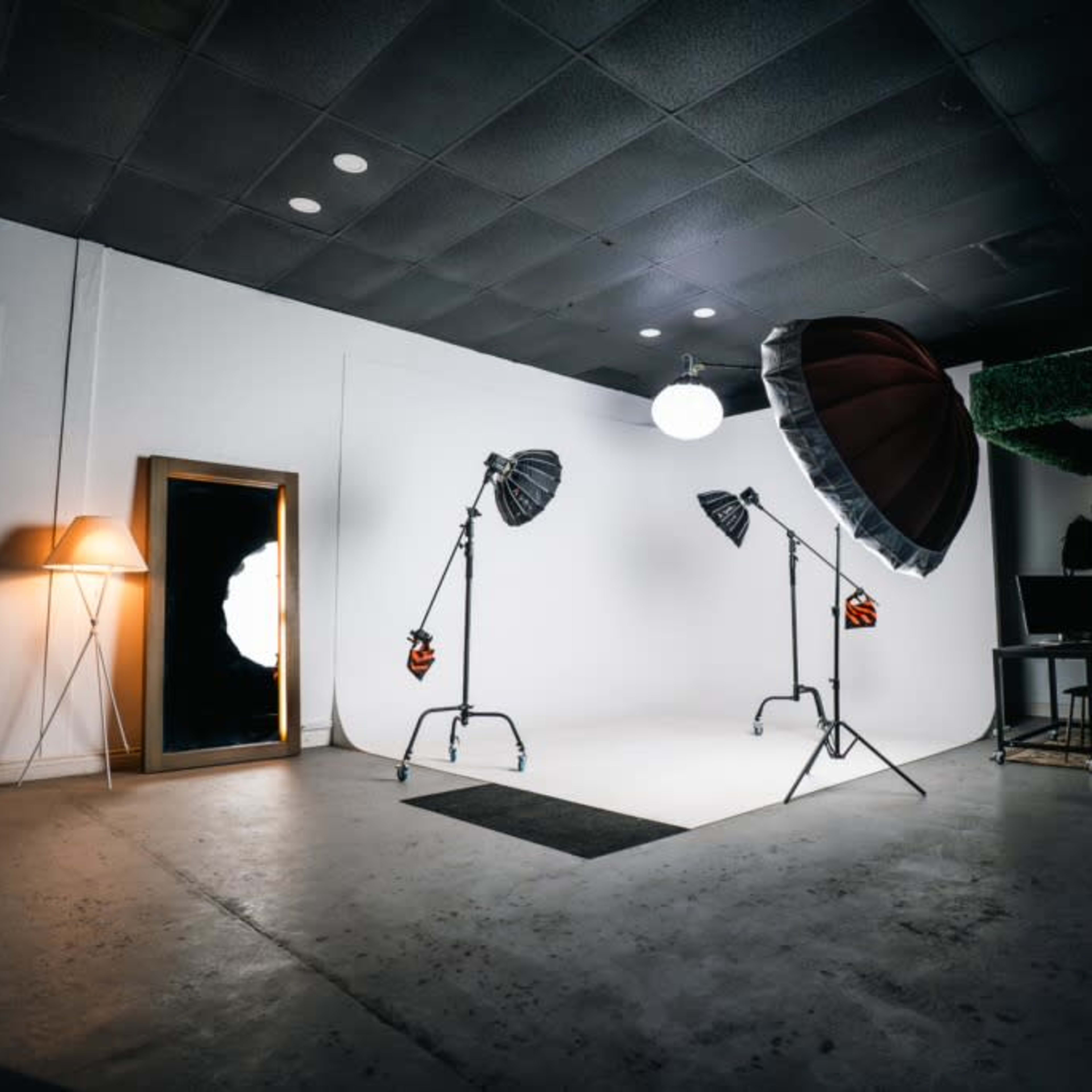 A photography studio featuring various lighting equipment, a large mirror, and a minimalist backdrop.