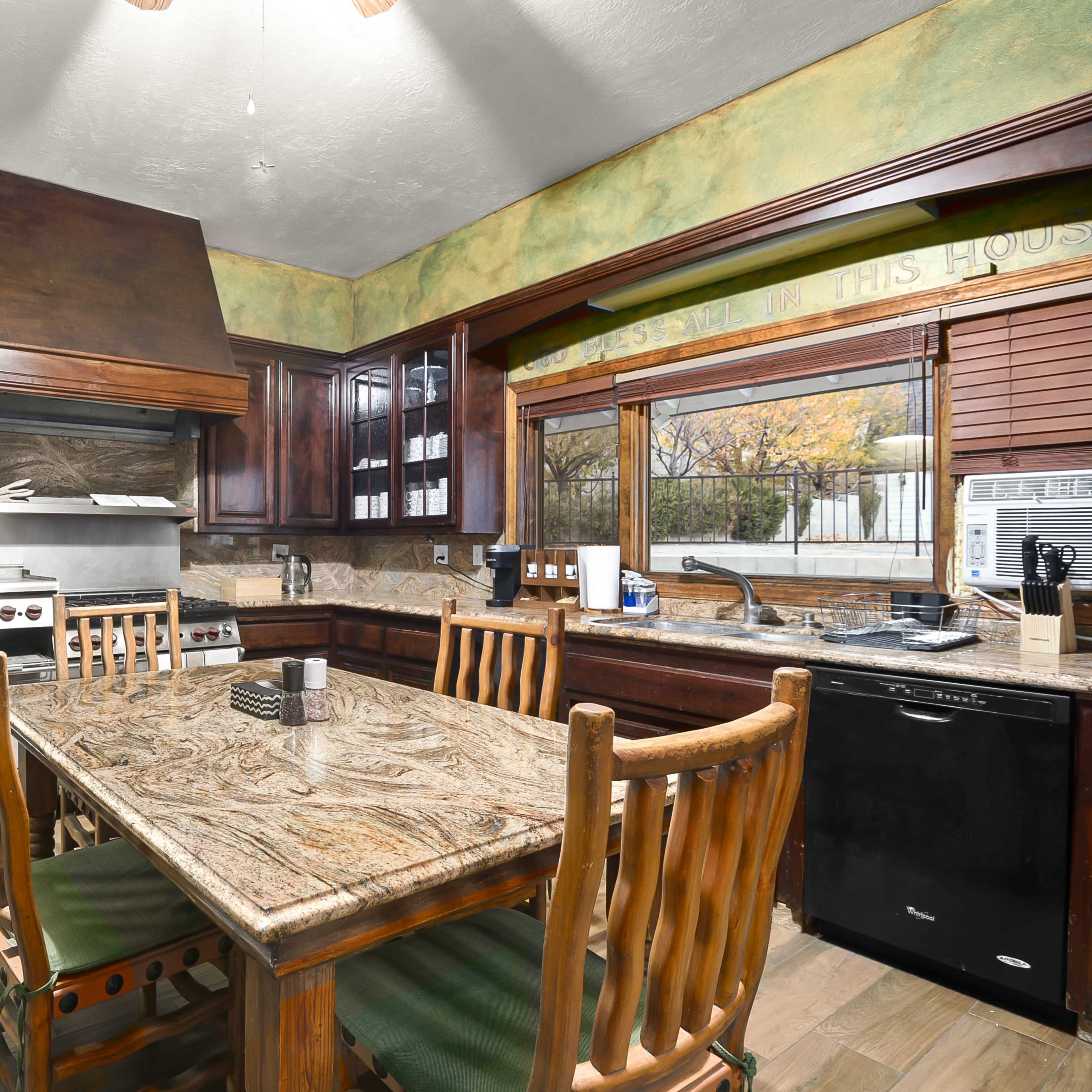 A kitchen with wooden cabinets, a large stone countertop, stainless steel appliances, and a dining table surrounded by wooden chairs.