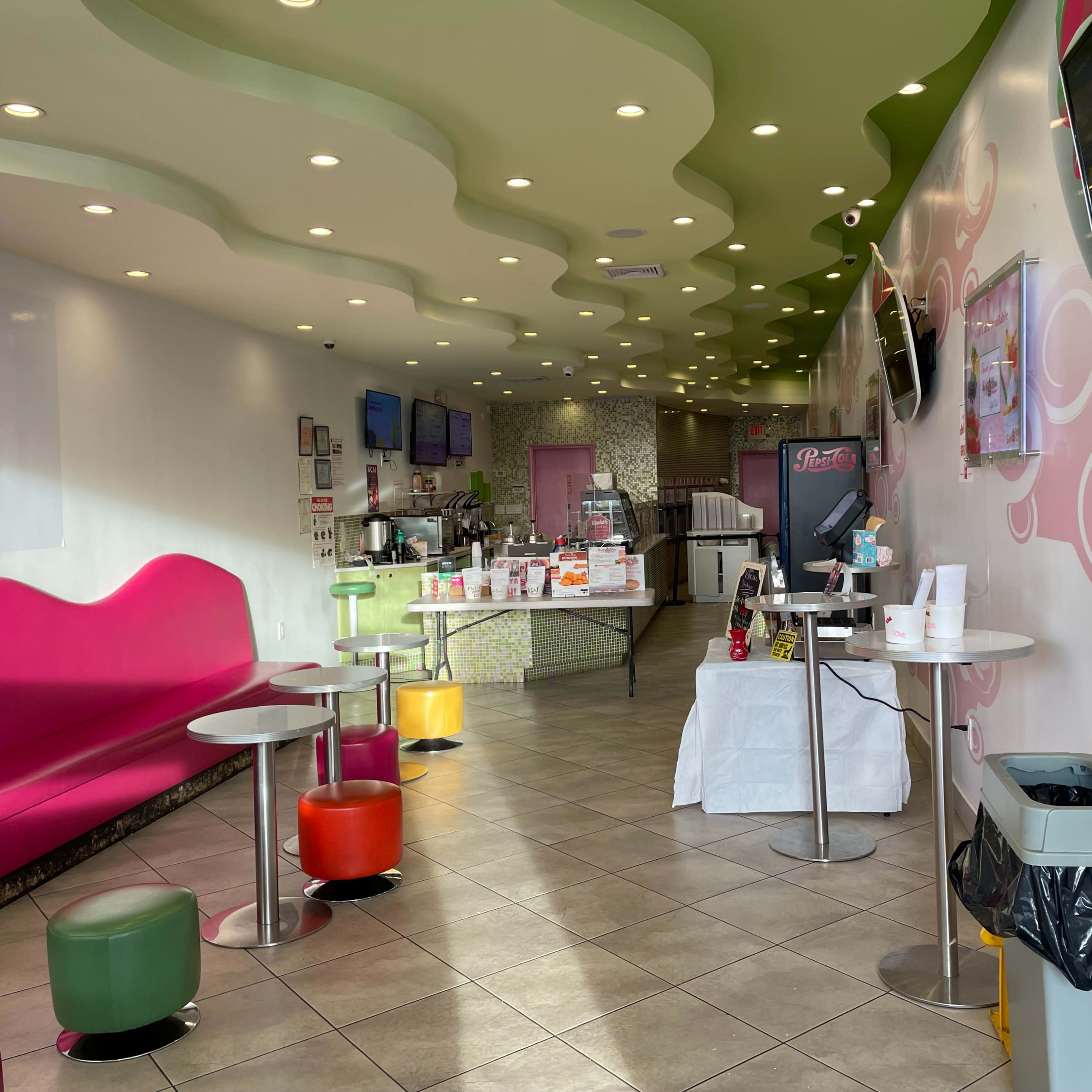 A colorful ice cream shop with curved ceilings, pink seating, and a clean, modern design featuring multiple screens and tables.