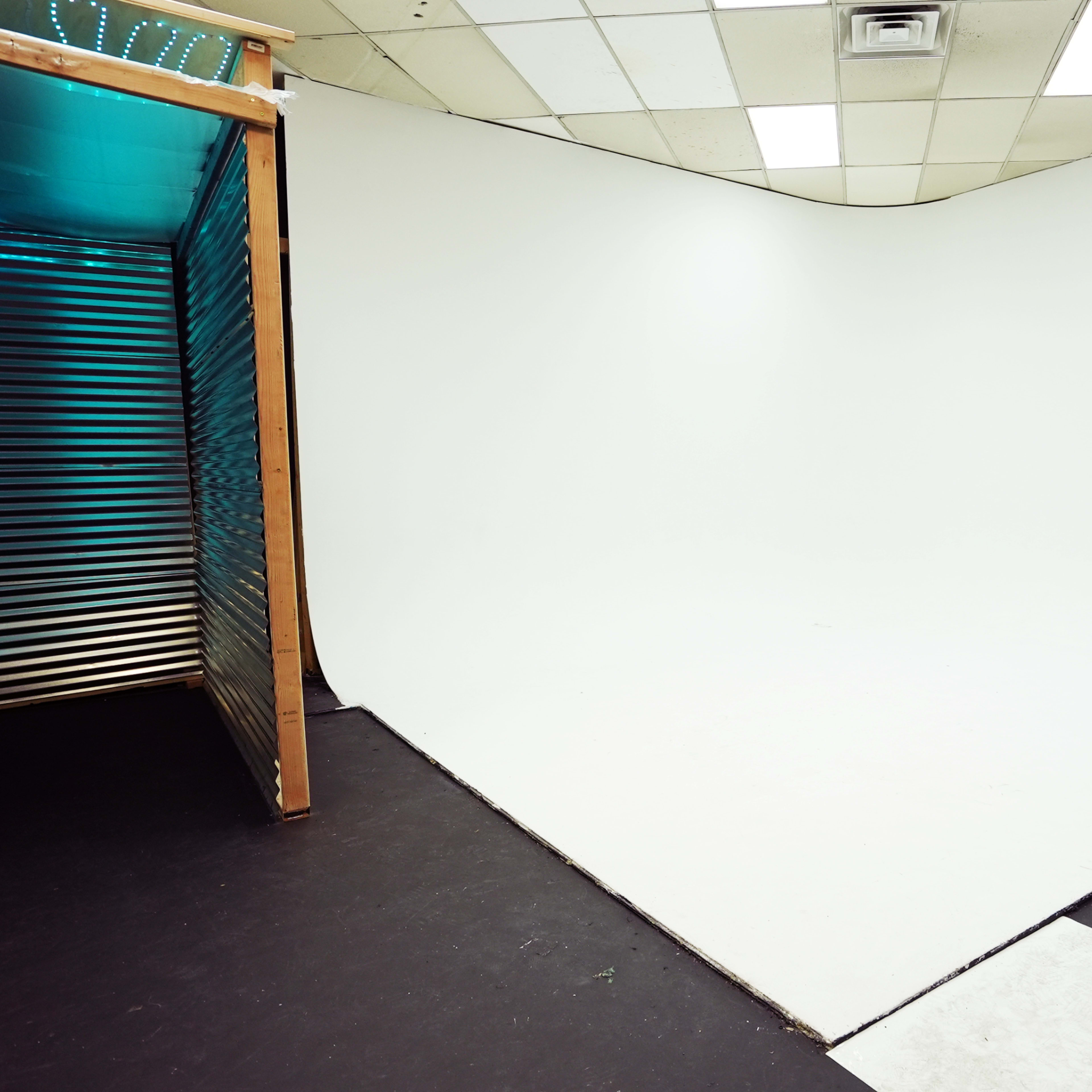 A photography studio with a seamless white backdrop and a corner entrance made of wood and metal.