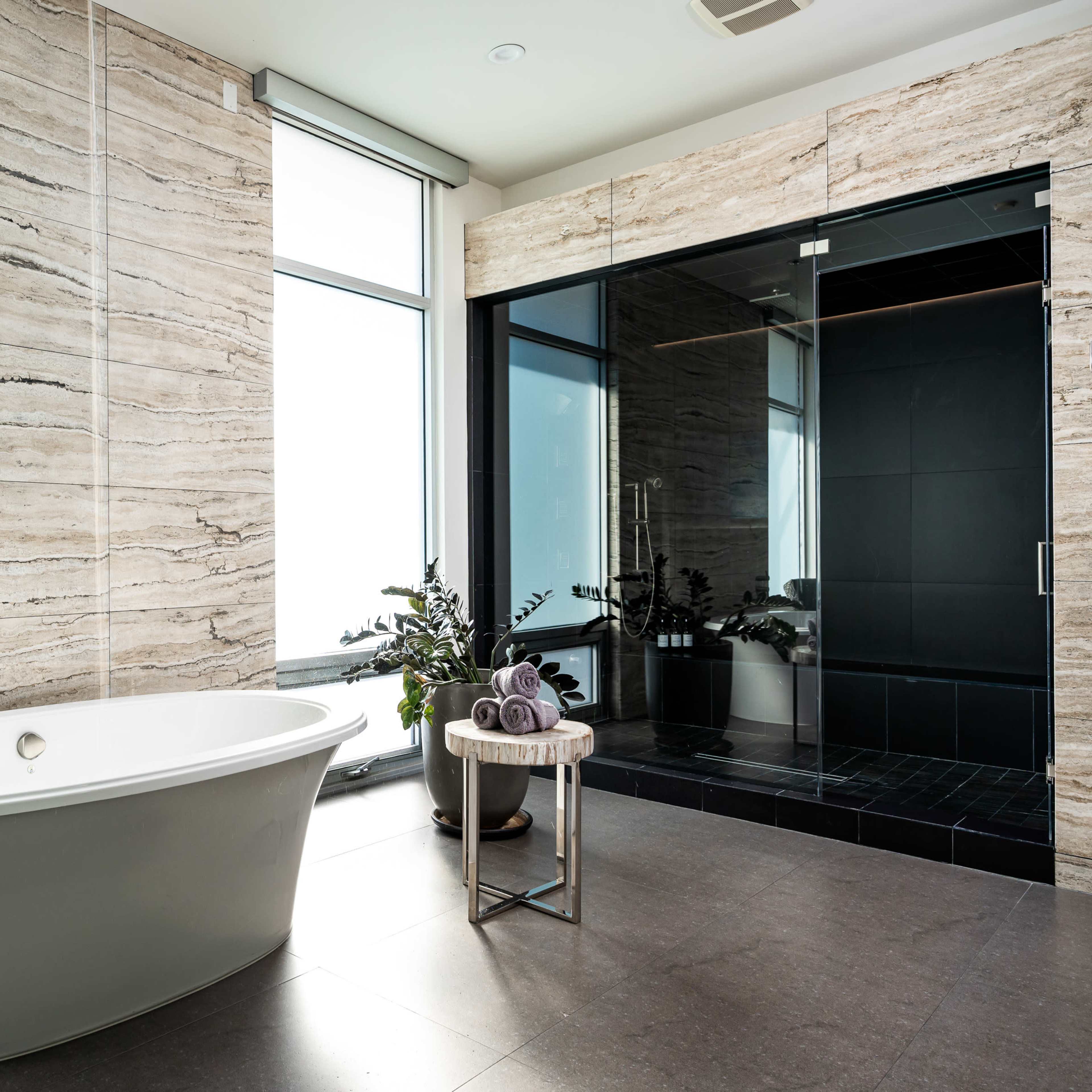 A modern bathroom features a freestanding bathtub next to a glass-enclosed shower and marble walls.