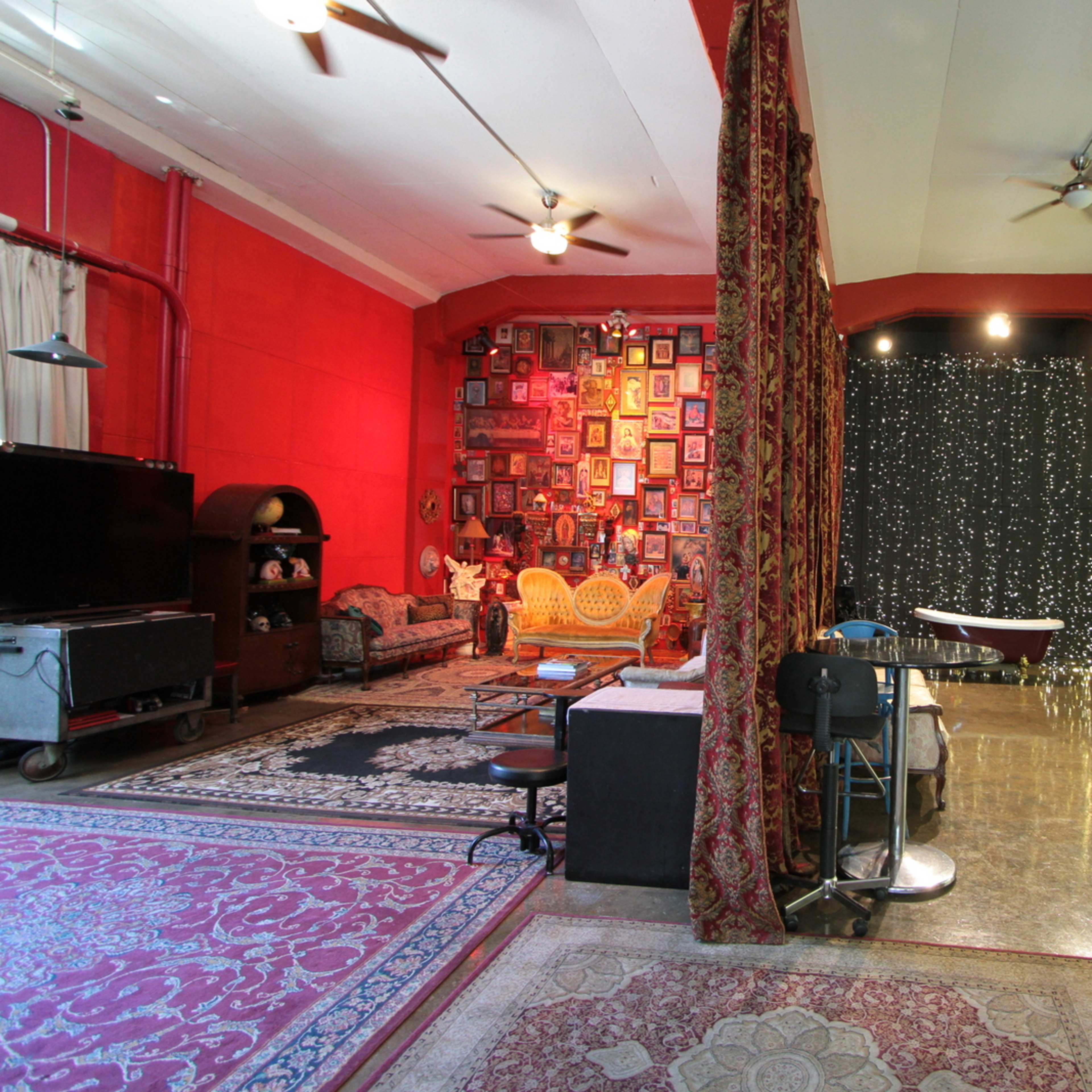 A spacious studio with red and black walls, featuring various decorations, seating areas, and photography equipment scattered throughout.
