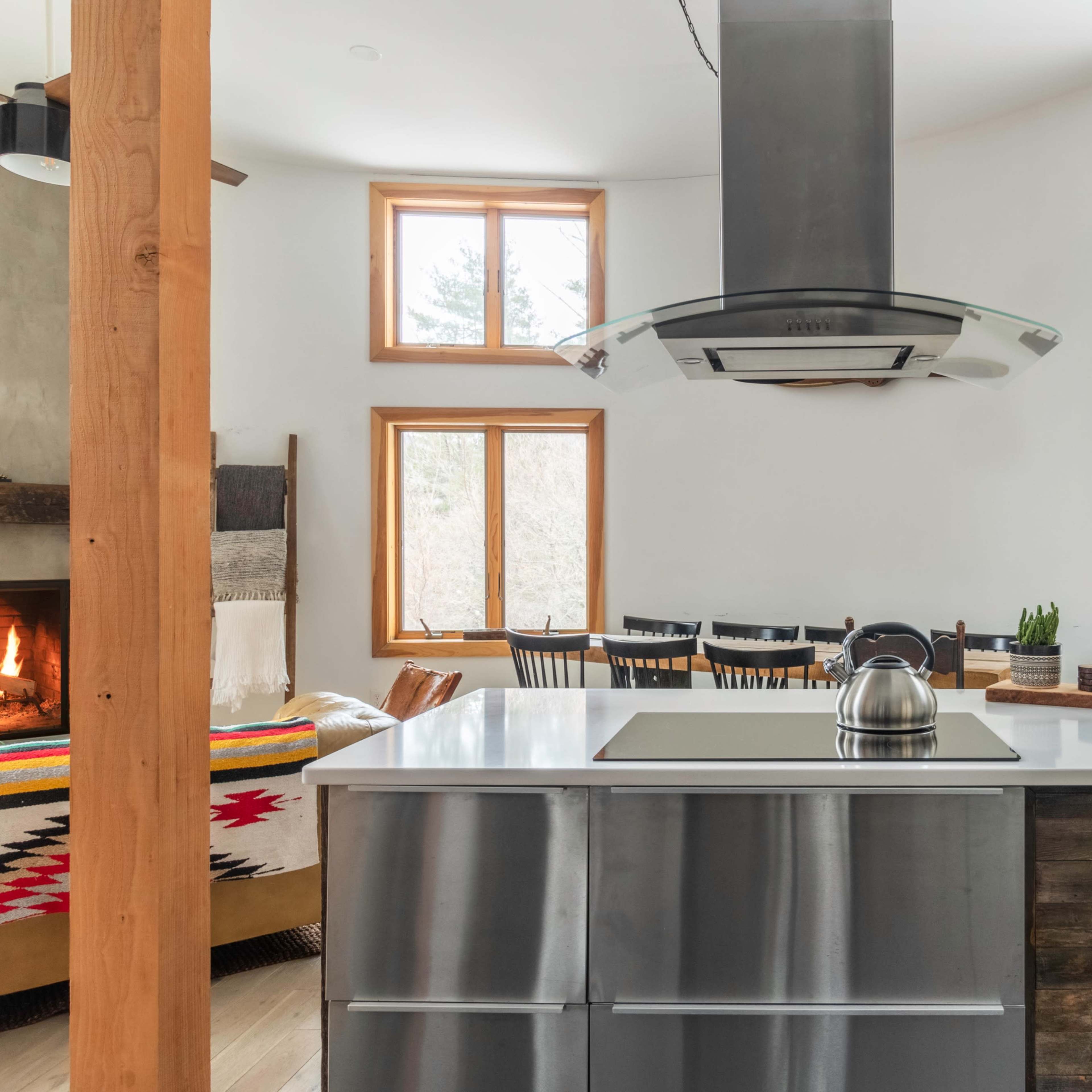 A modern kitchen features a central stovetop island with a hood, large windows, and a cozy seating area with a fireplace.