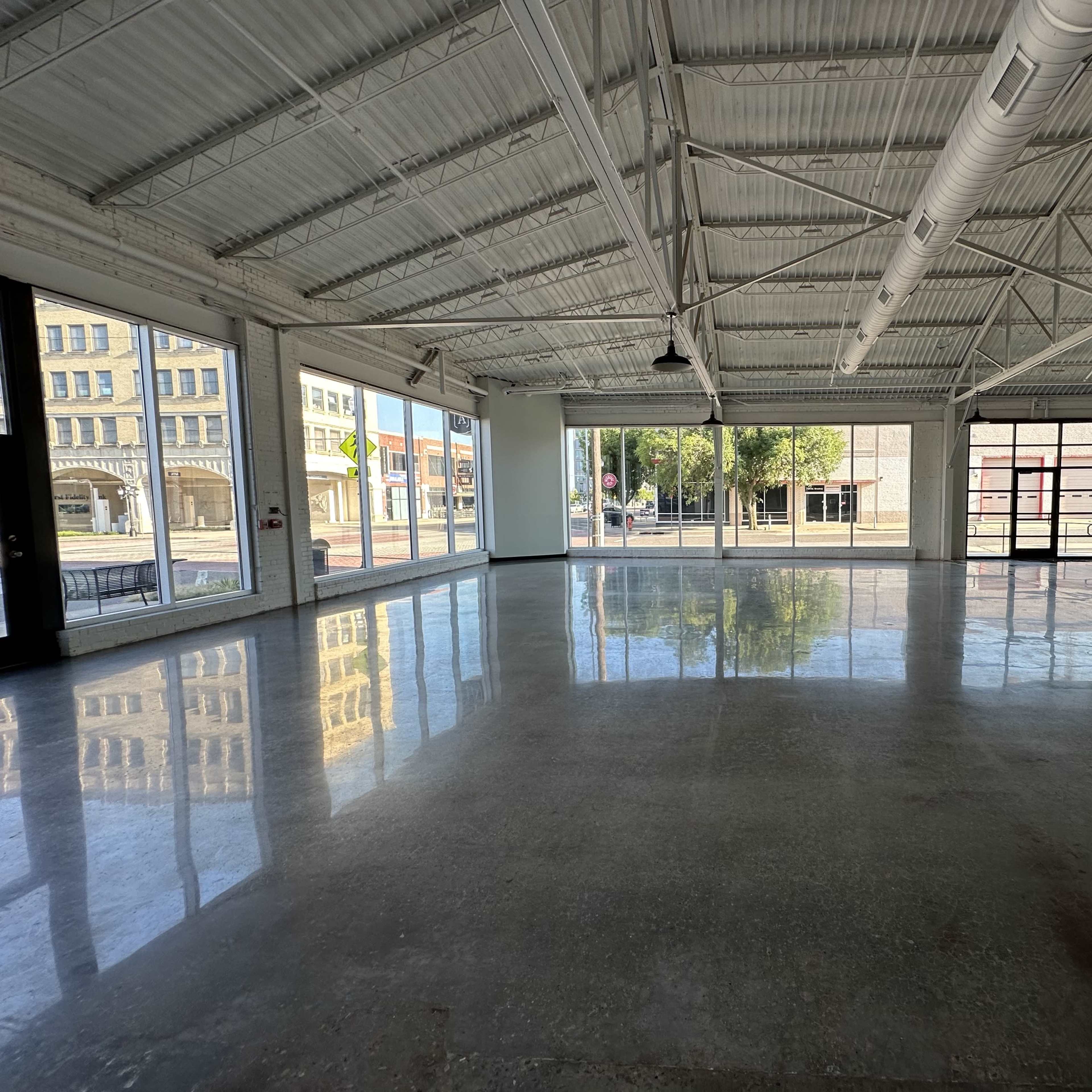 A spacious, empty room with polished concrete floors, large windows, and a high ceiling.