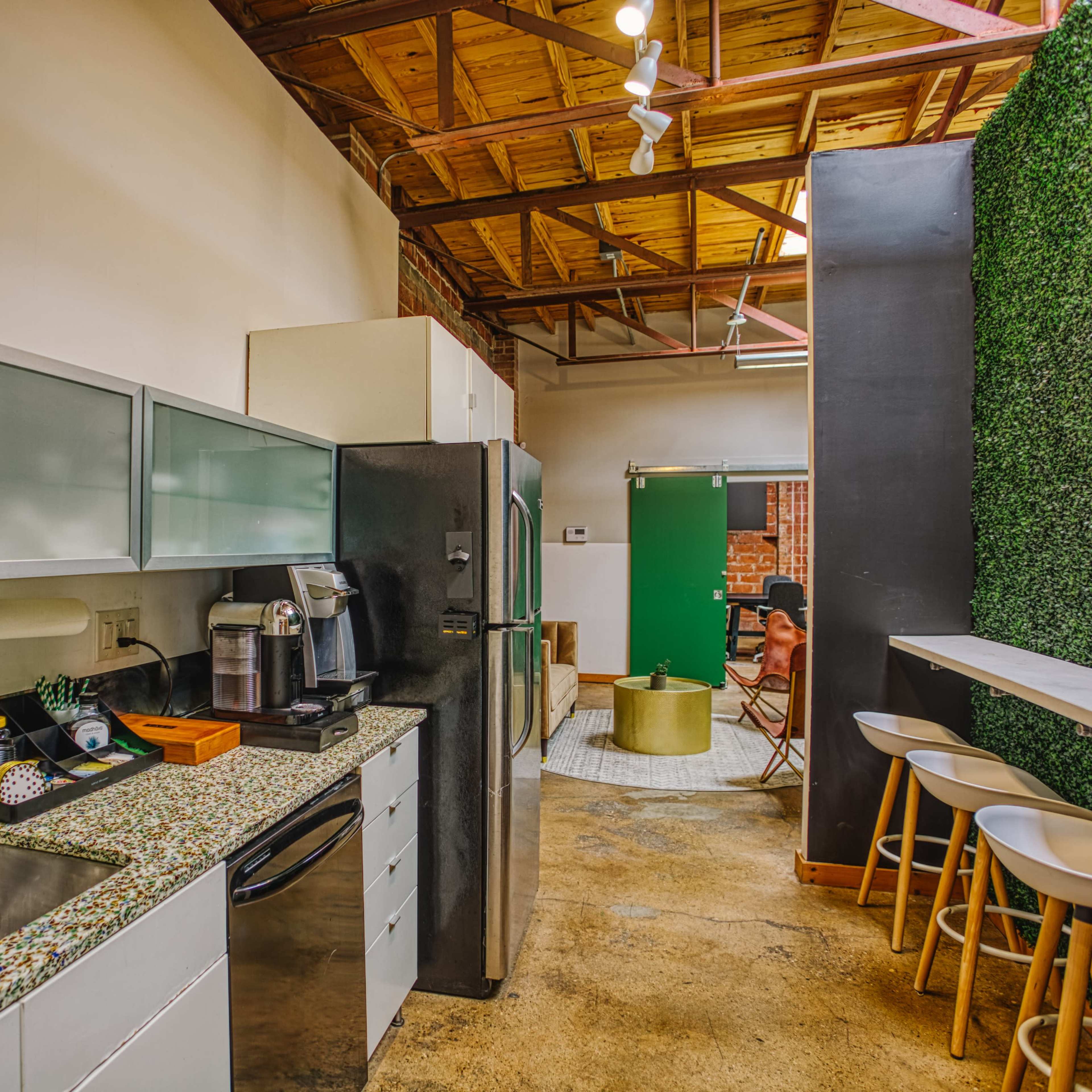 A modern kitchen space with a green accent wall, stainless steel appliances, and a countertop with seating.