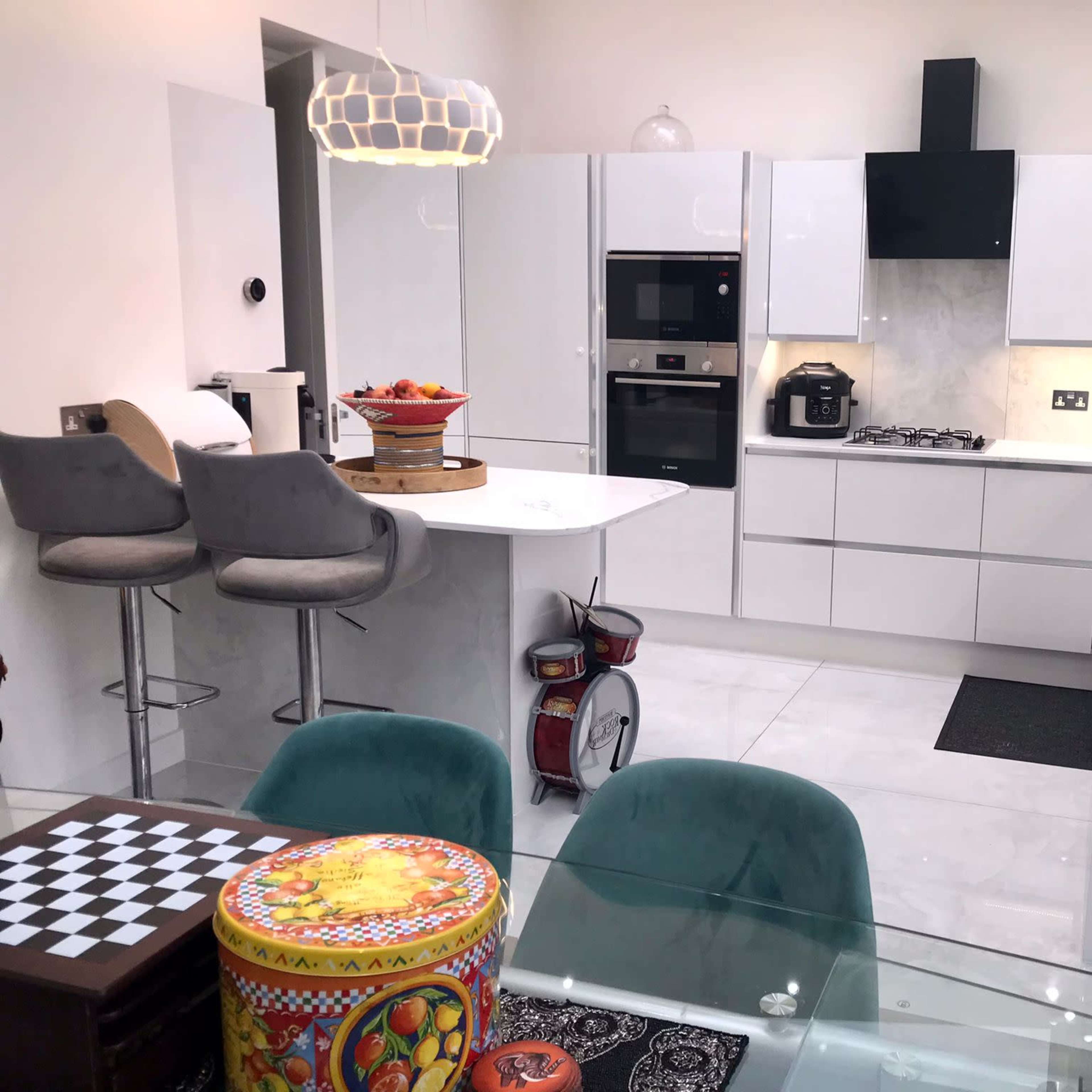 A modern kitchen with white cabinetry, sleek appliances, a dining area featuring a glass table, and decorative items like a checkered board and colorful containers.