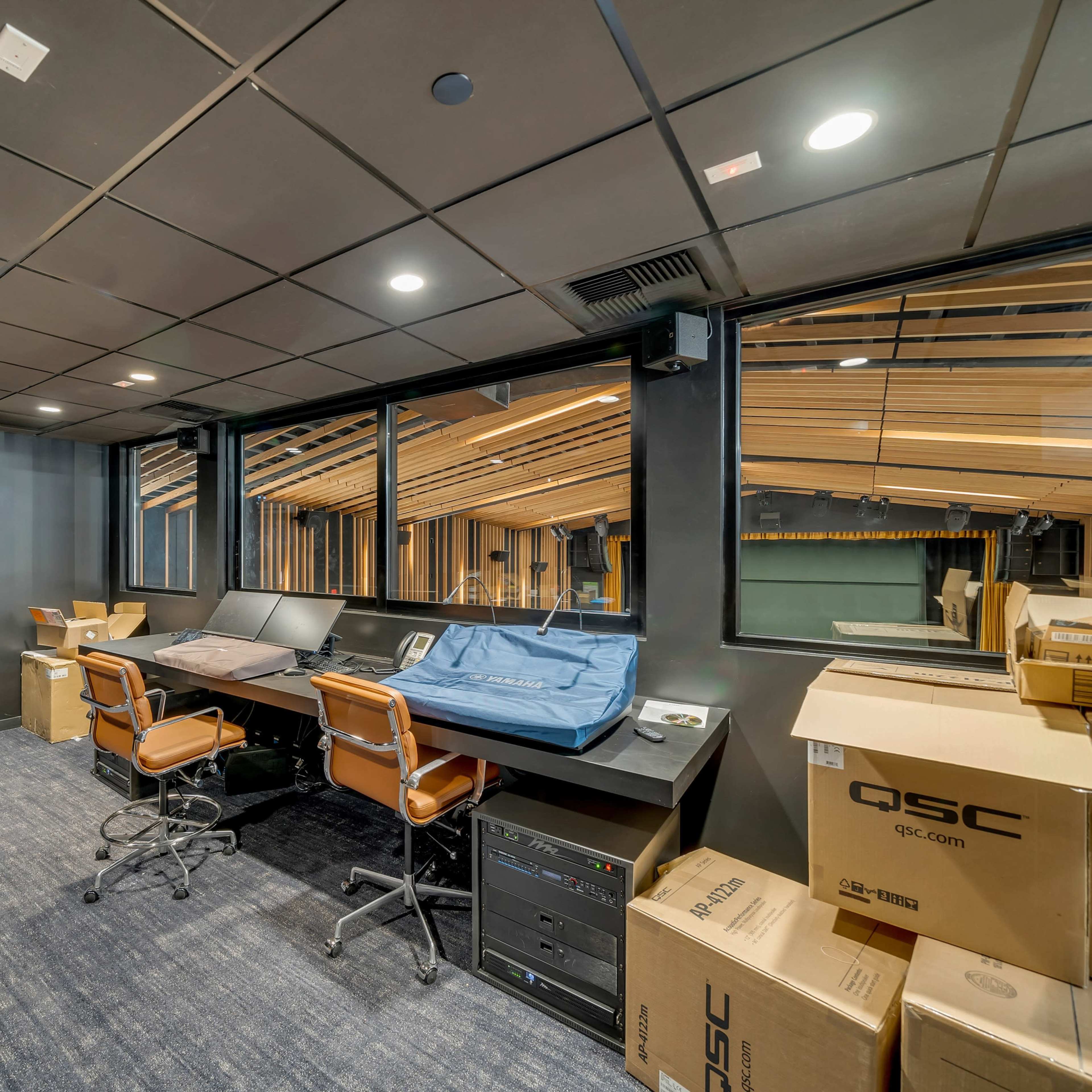 A dimly lit room with two desks equipped with computers and stacked boxes against the walls.