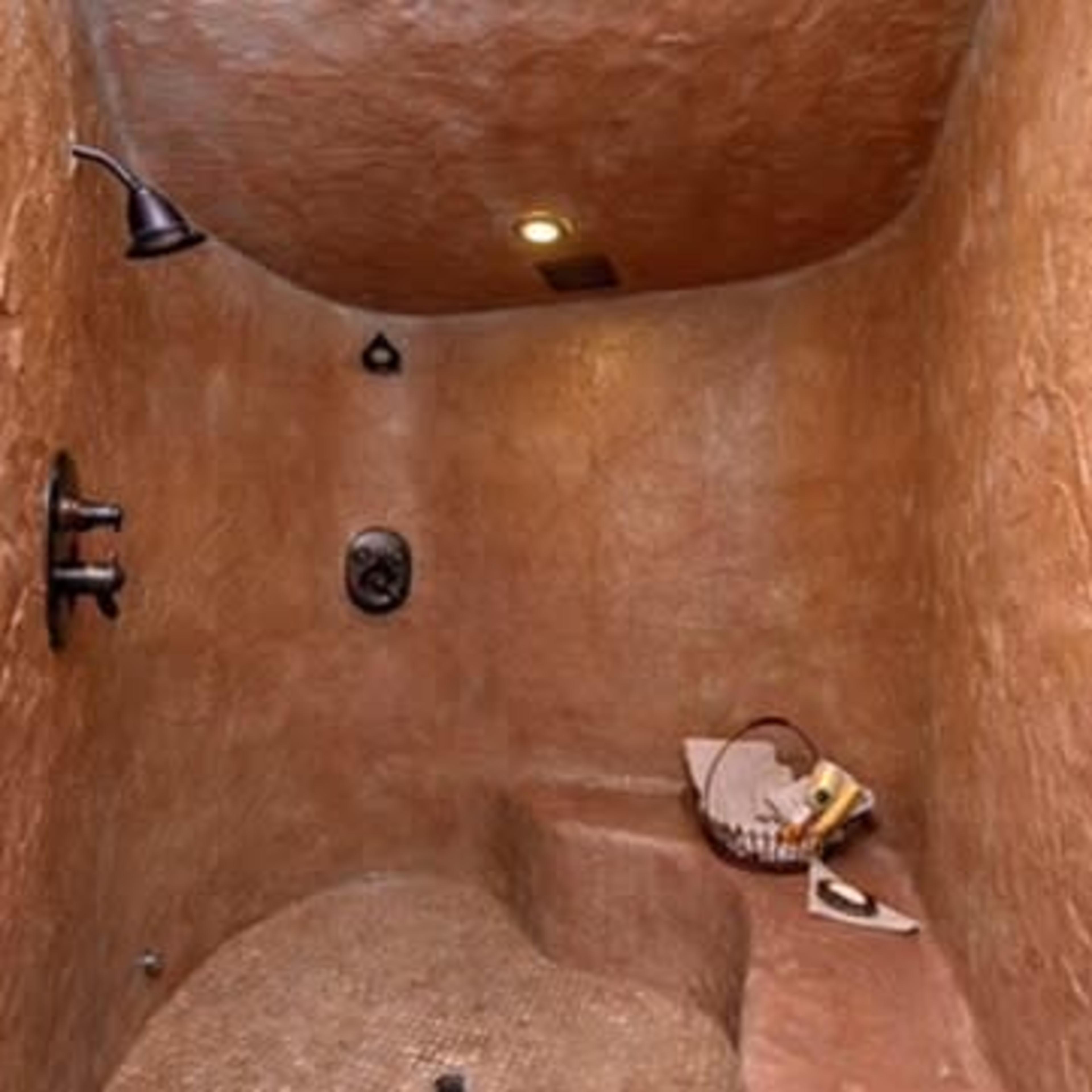 A small, curved shower area with textured walls and a bench, featuring a showerhead and fixtures on one side.
