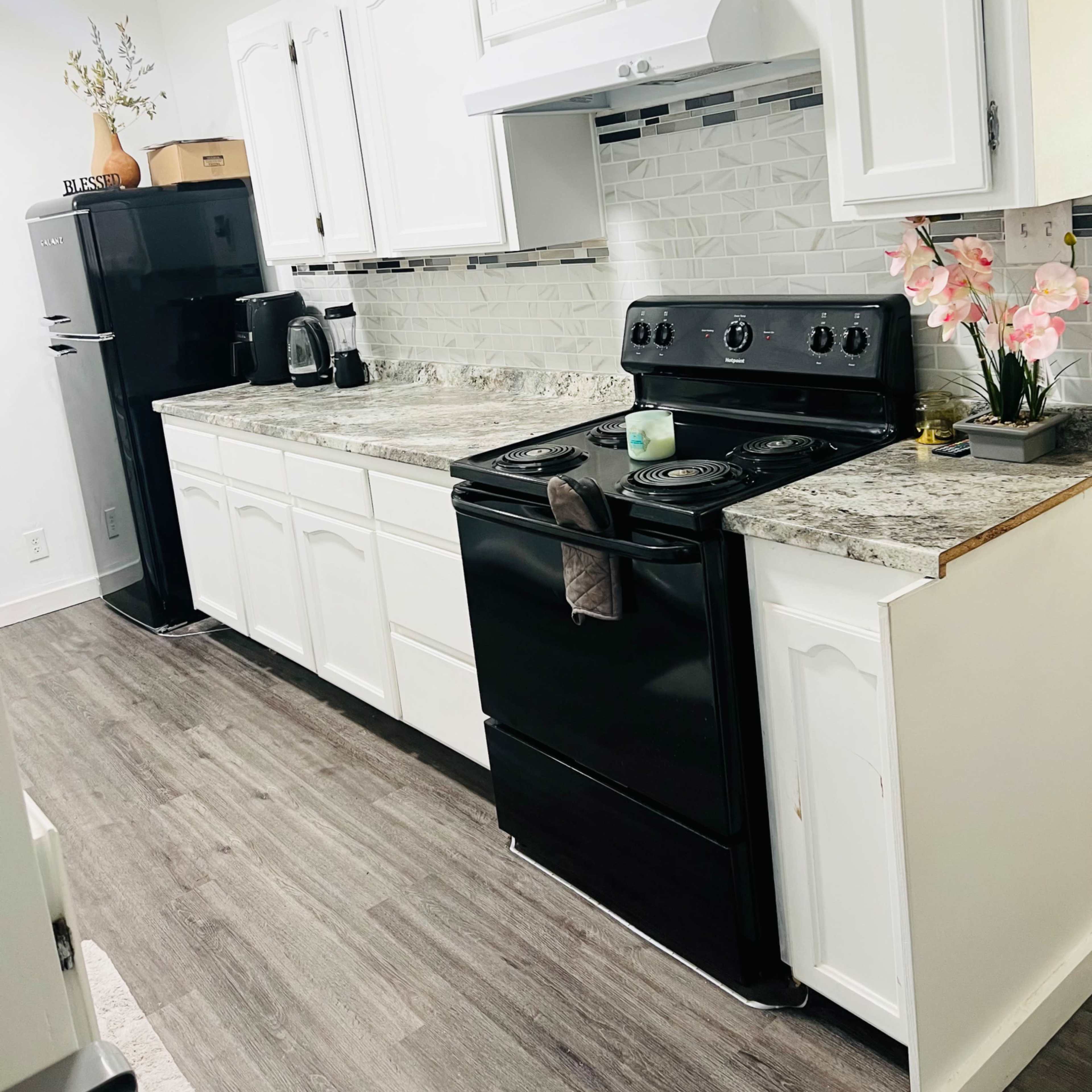 A kitchen with white cabinets, a black stove, and a dark refrigerator, set against light-colored backsplash tiles and a granite countertop.