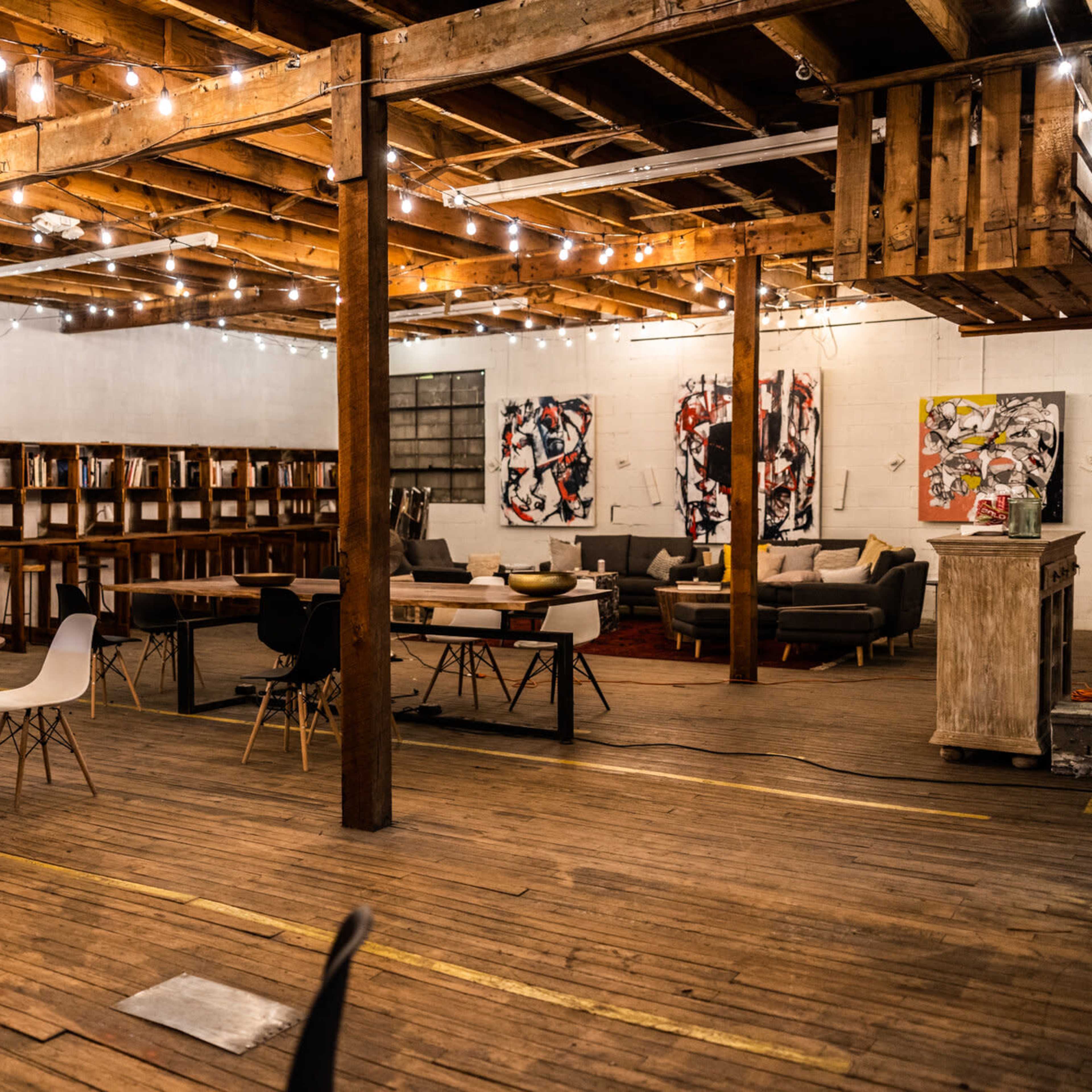 An industrial-style open space with wooden floors, exposed beams, and various seating arrangements surrounded by artwork on the walls.