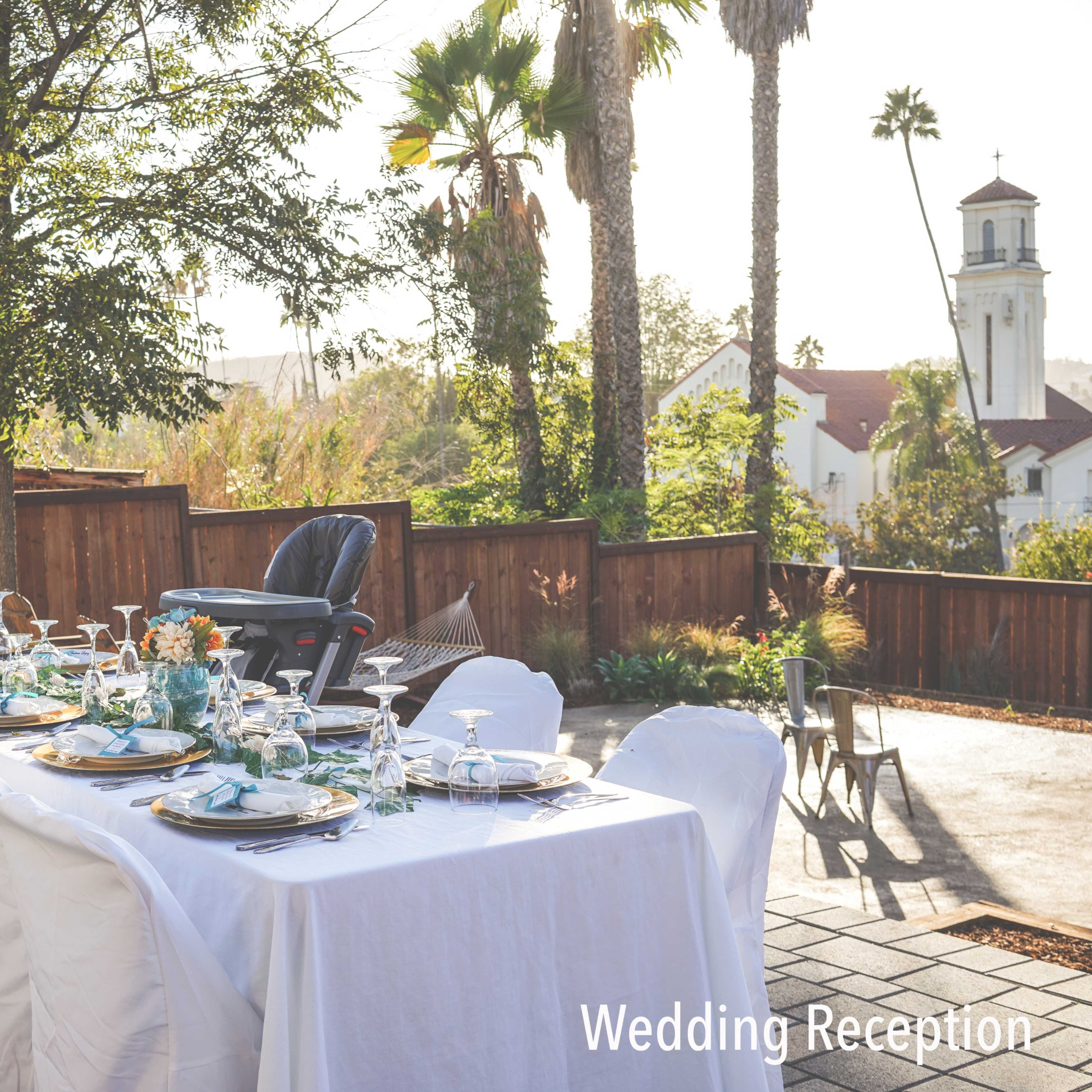 A long table set with plates, glassware, and floral centerpieces is arranged for a wedding reception in an outdoor setting.
