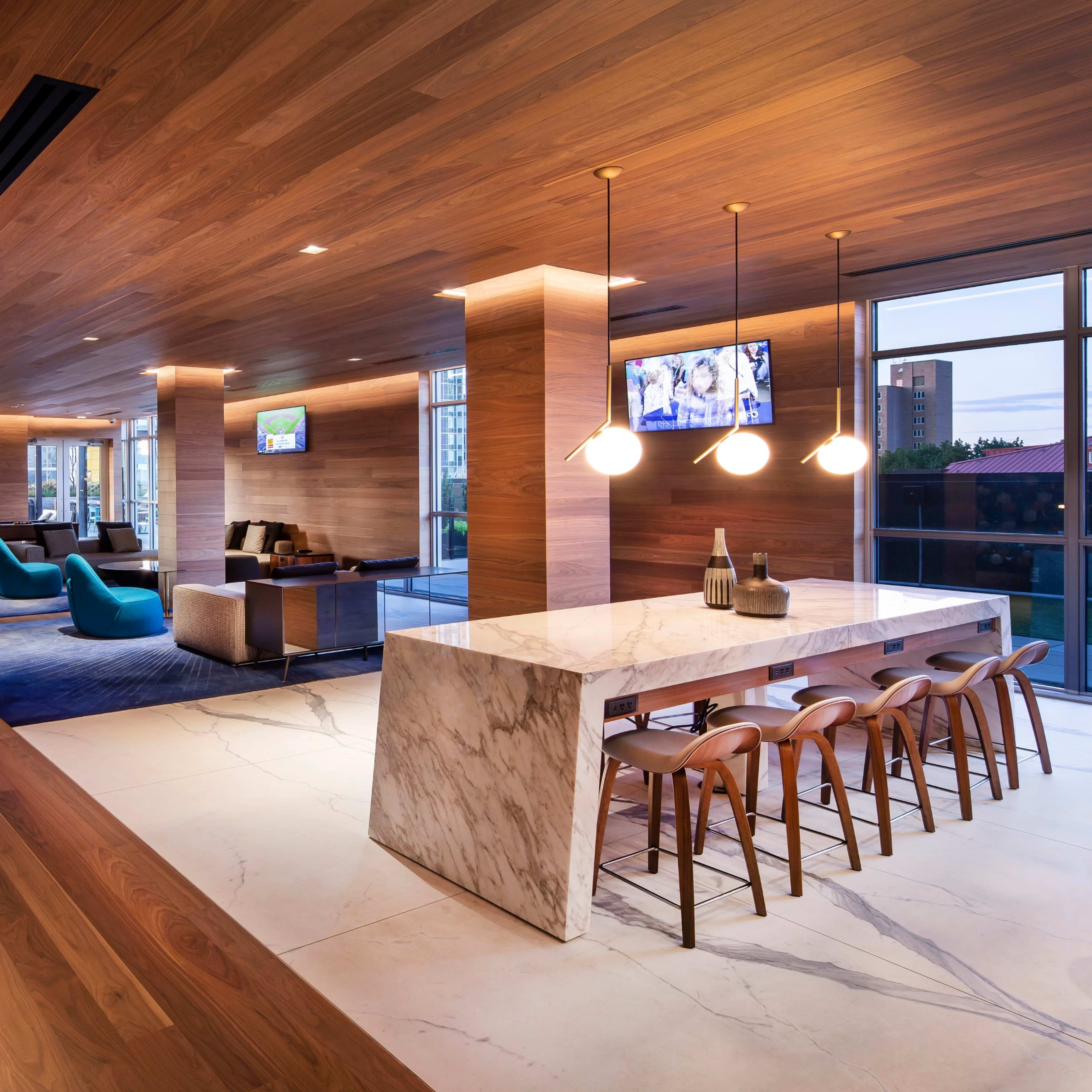 A modern lounge area with wooden walls, a marble bar, and various seating arrangements, including a wall adorned with colorful paper squares.