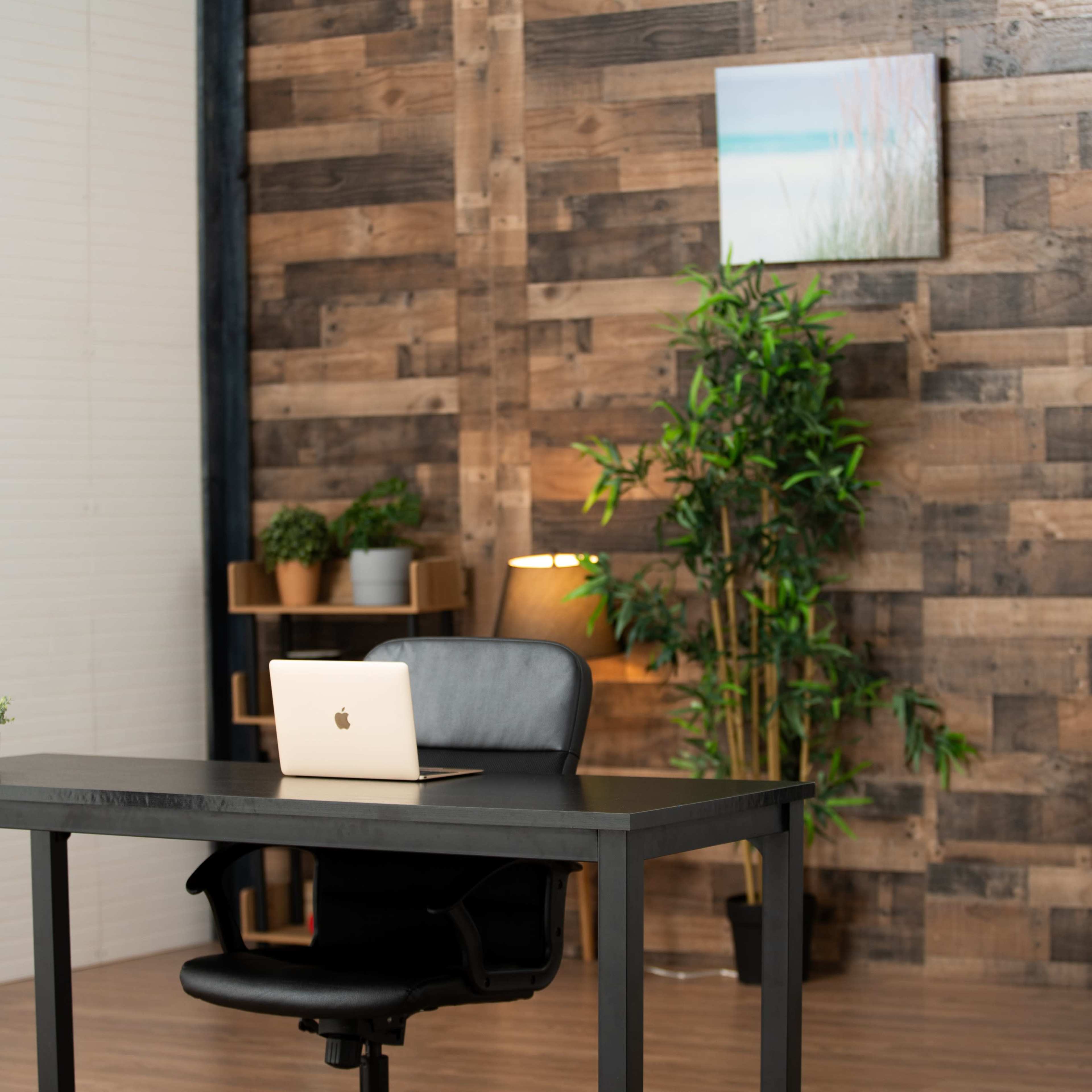 A modern office space features a desk with a laptop, a black chair, and green plants against a wooden wall.