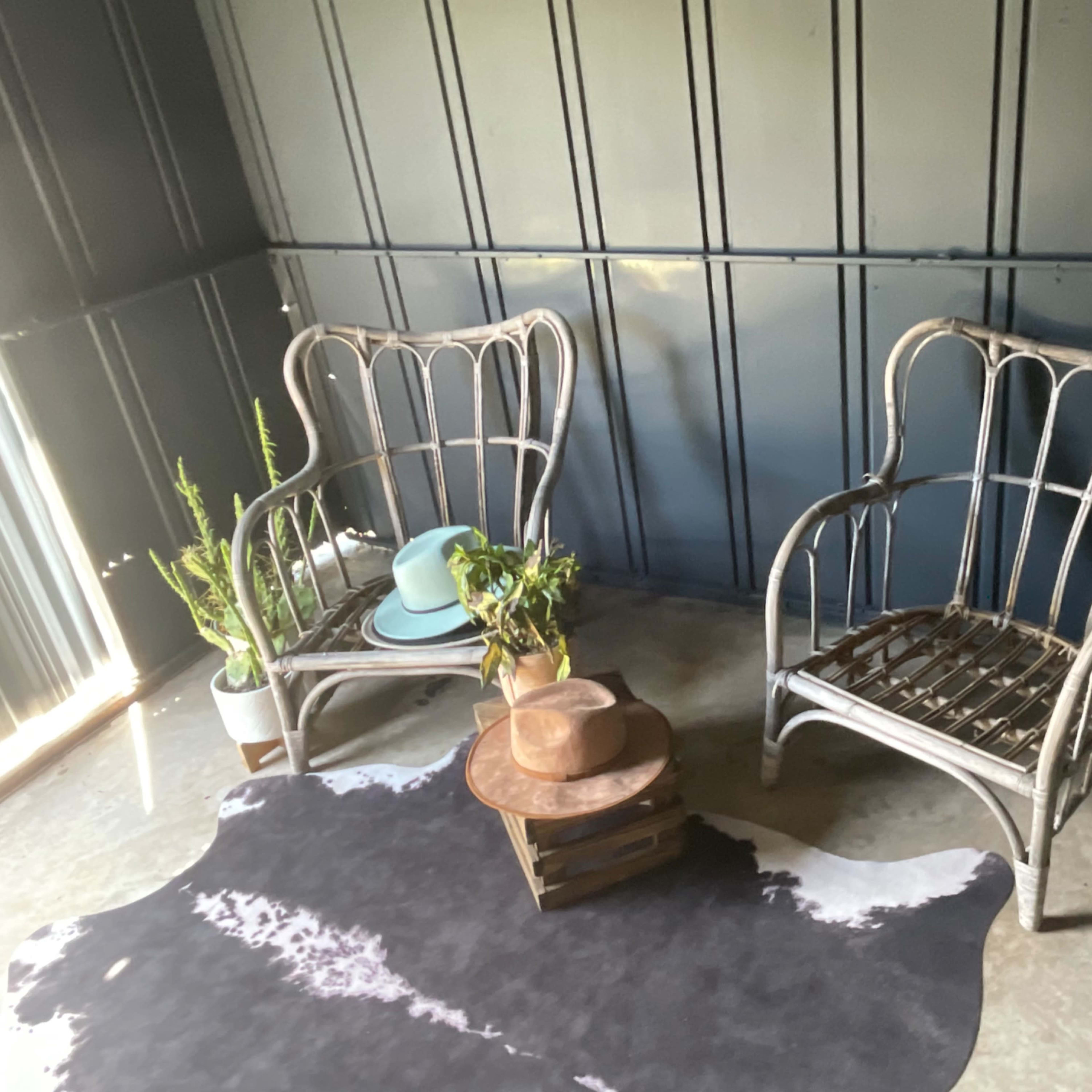 Two wicker chairs are positioned across from each other around a small, rustic table on a cowhide rug in a room with dark blue walls.