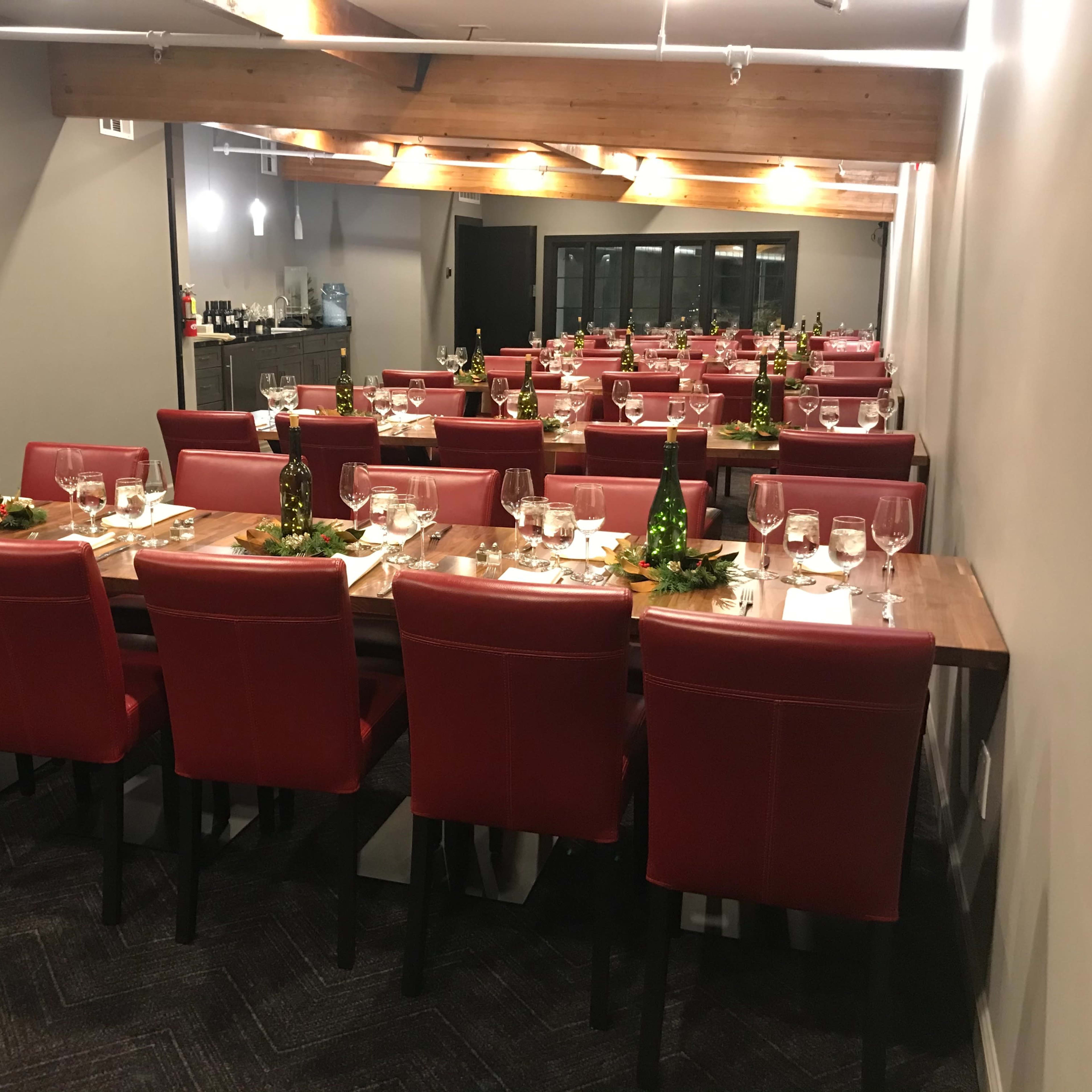 A spacious dining room is set with long wooden tables arranged for a formal meal, featuring red chairs and elegant table settings.
