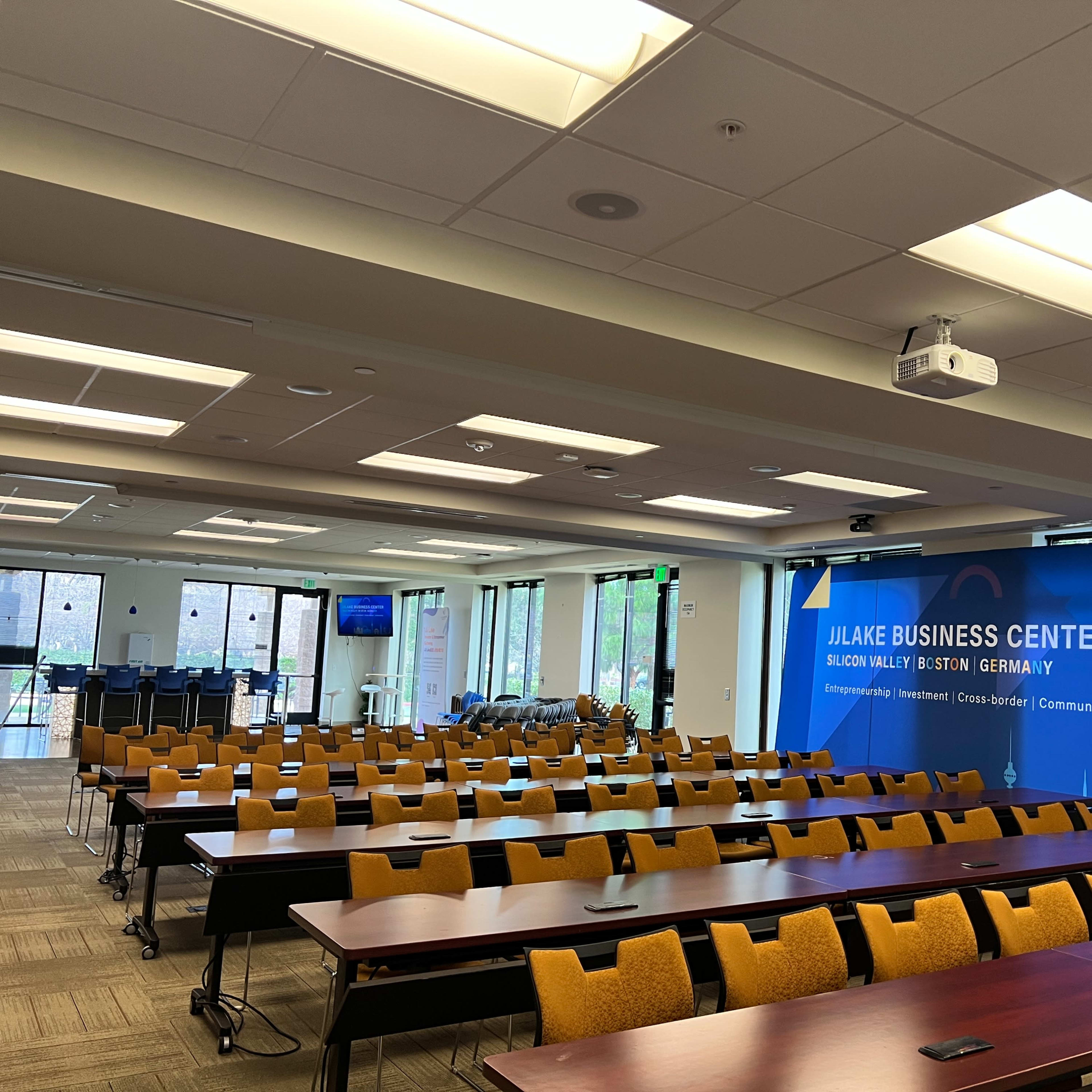 A spacious conference room with rows of tables and chairs, featuring a large banner displaying "Jilake Business Center."