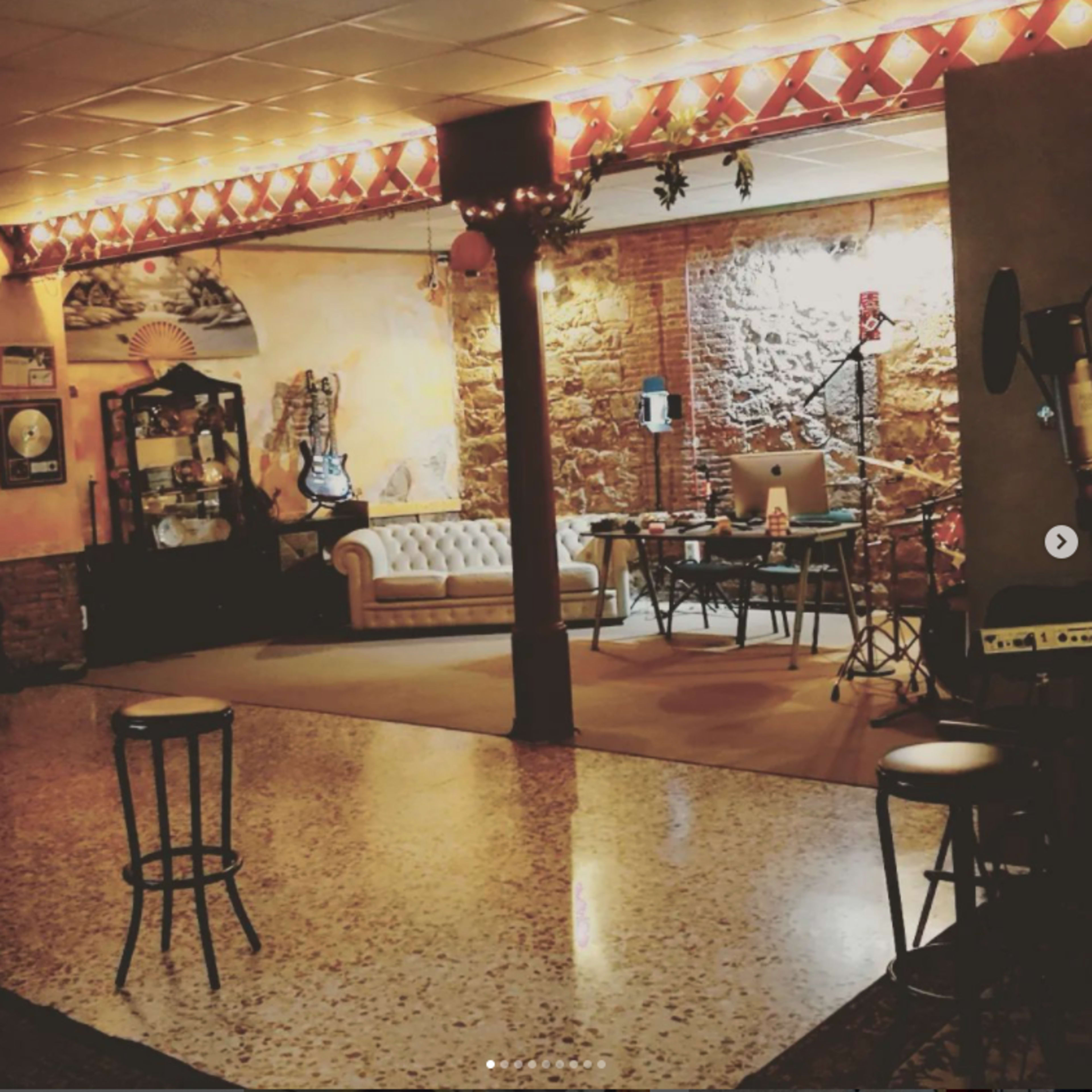 A cozy music studio with a couch, a desk with equipment, and musical instruments arranged against a textured brick wall.