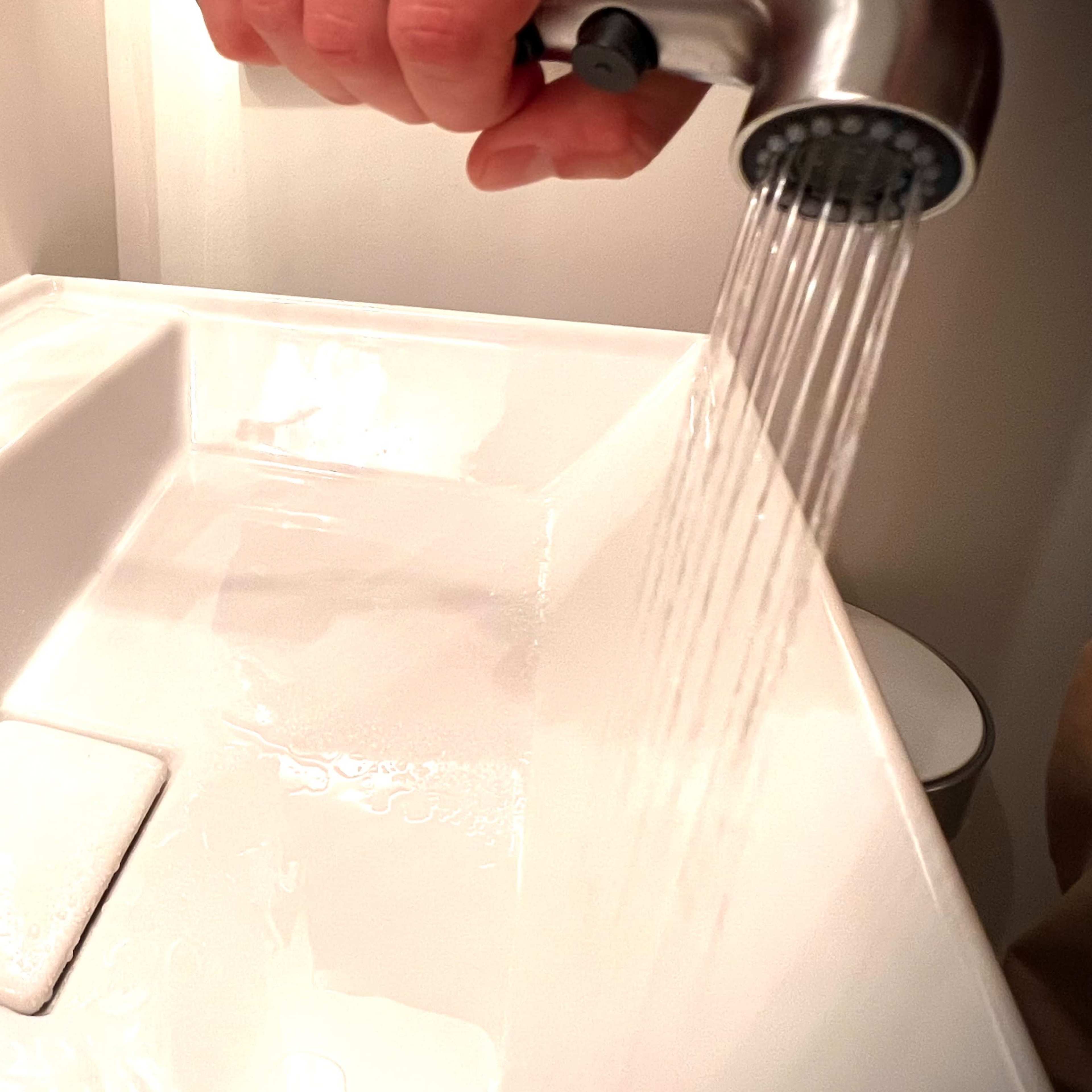 A hand is turning on a faucet above a white sink, causing water to flow into the basin.