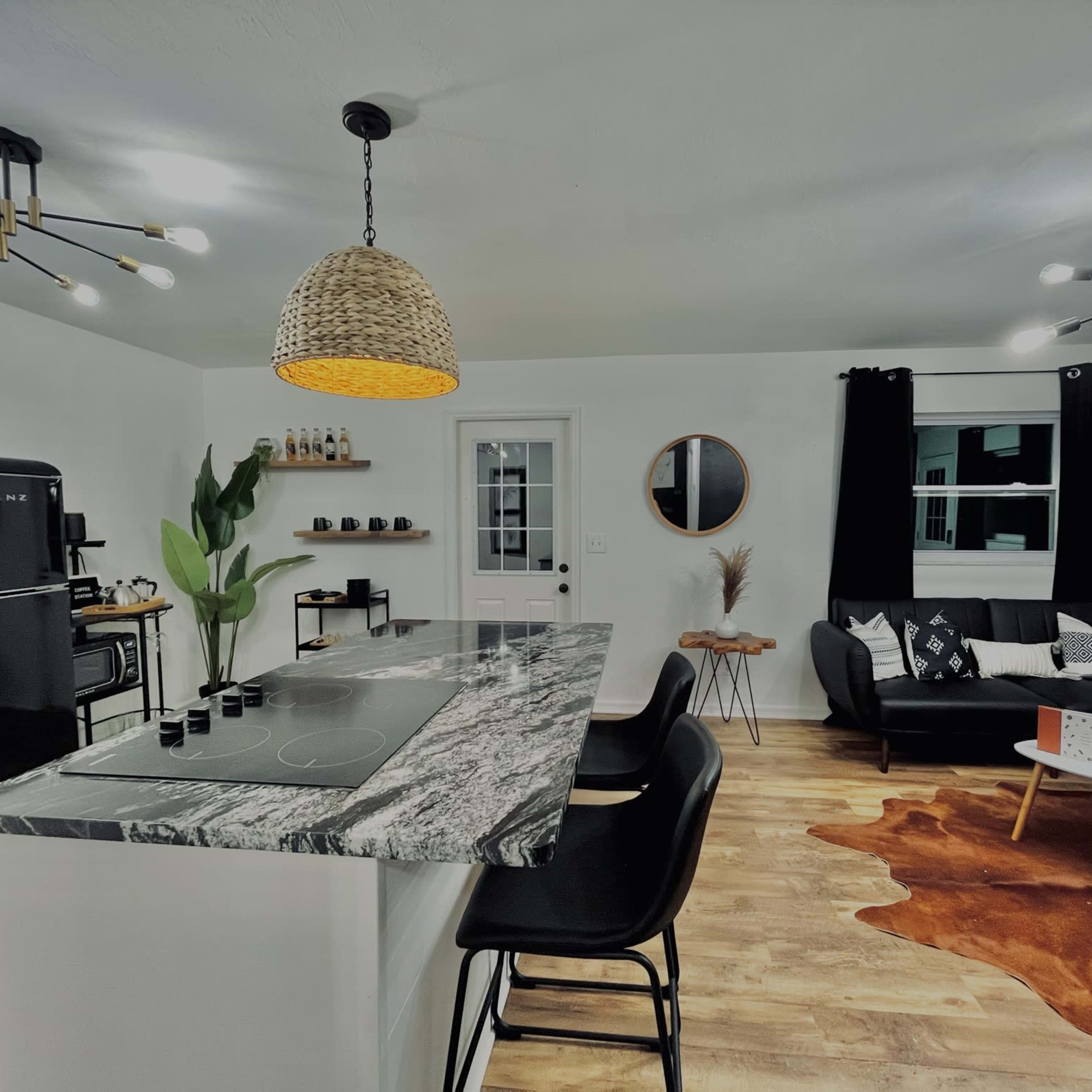 A modern kitchen and living area feature a marble countertop island, black chairs, a retro fridge, and a combination of dark and light decor.