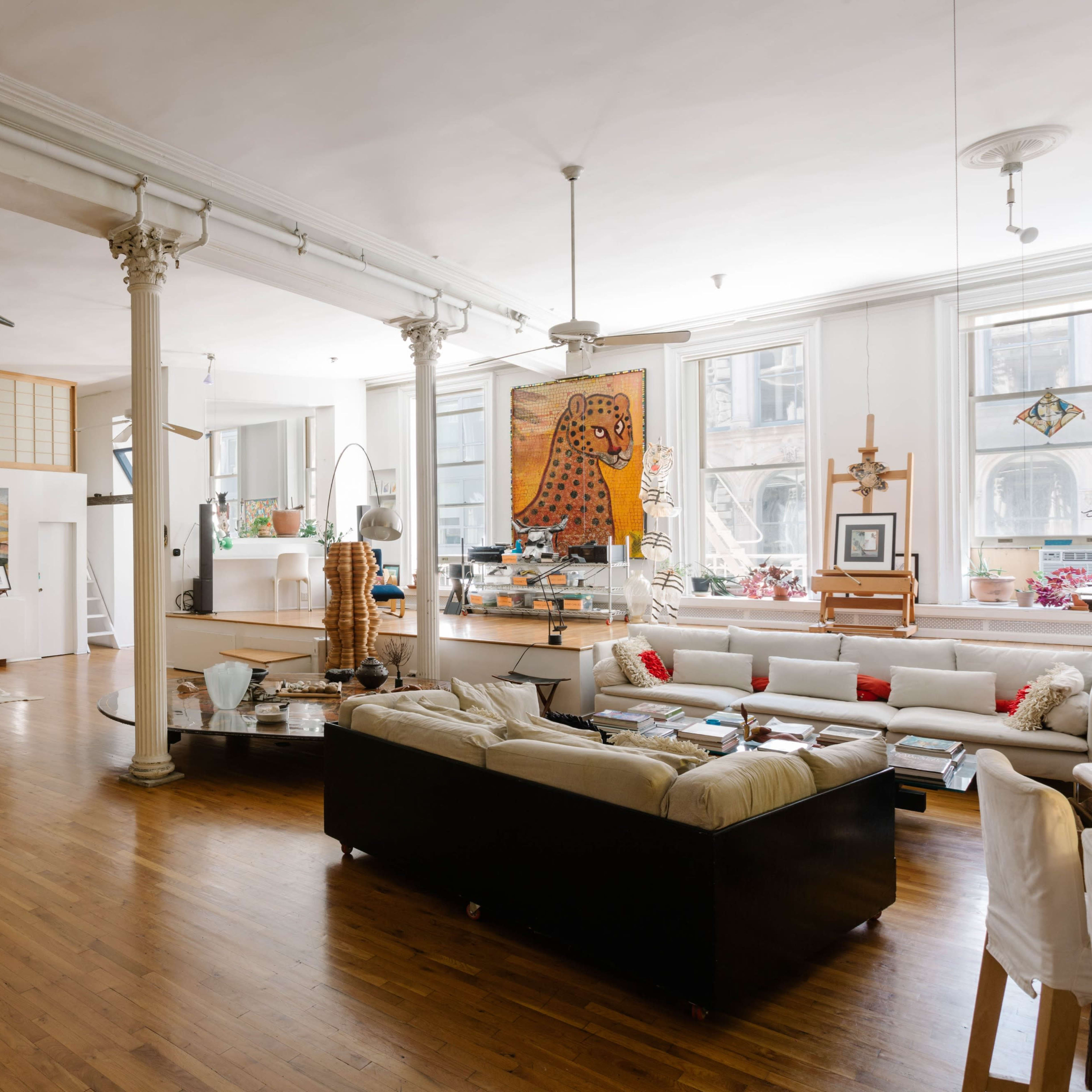 The spacious interior features wooden flooring, tall pillars, and a mix of modern and eclectic furniture, including a grand piano and artwork on the walls.