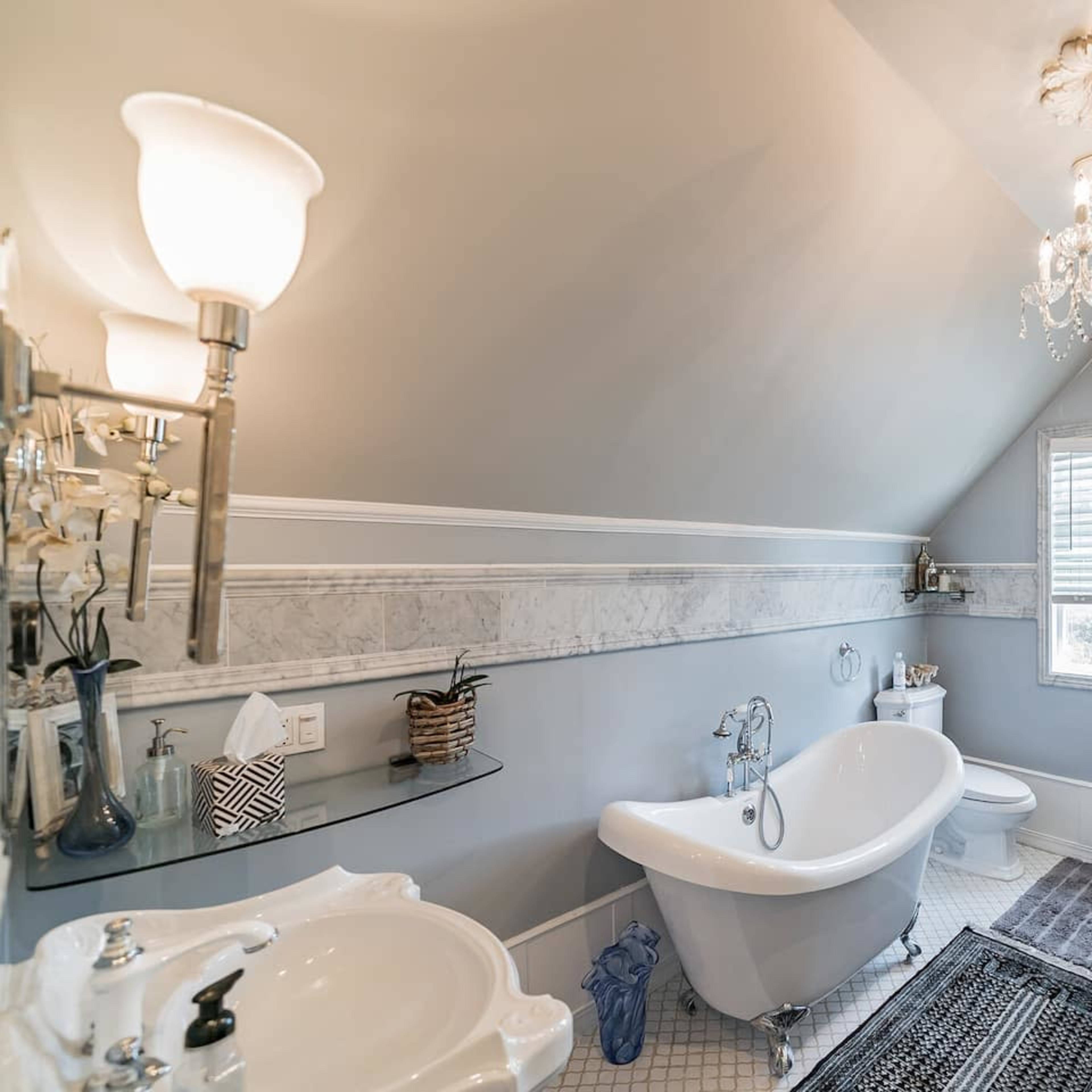 The bathroom features a clawfoot tub, a glass-enclosed shower, and a marble accent wall with modern fixtures.