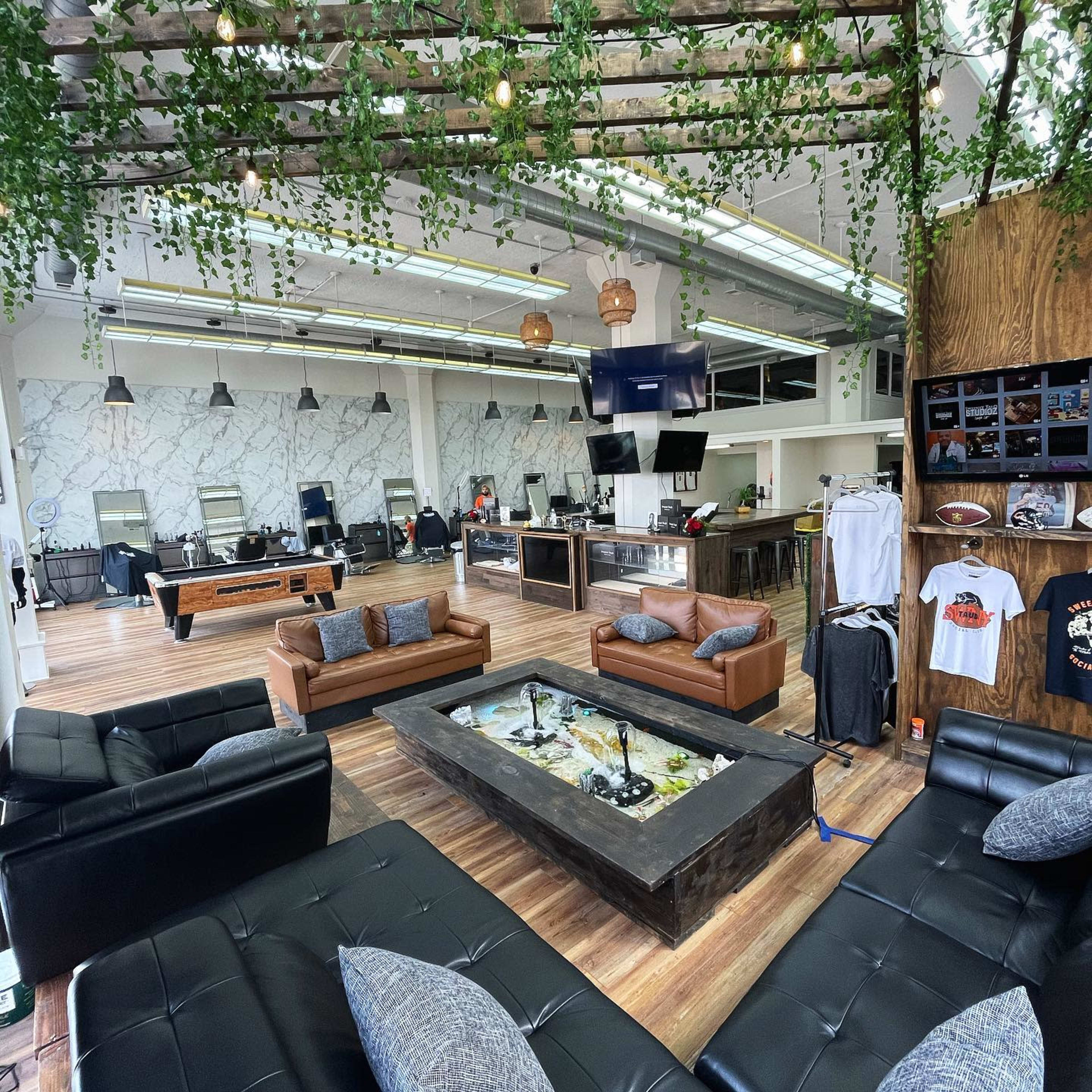 A spacious lounge area with leather couches, a unique coffee table with a built-in aquarium, and various recreational facilities in a modern interior featuring marble walls and greenery overhead.