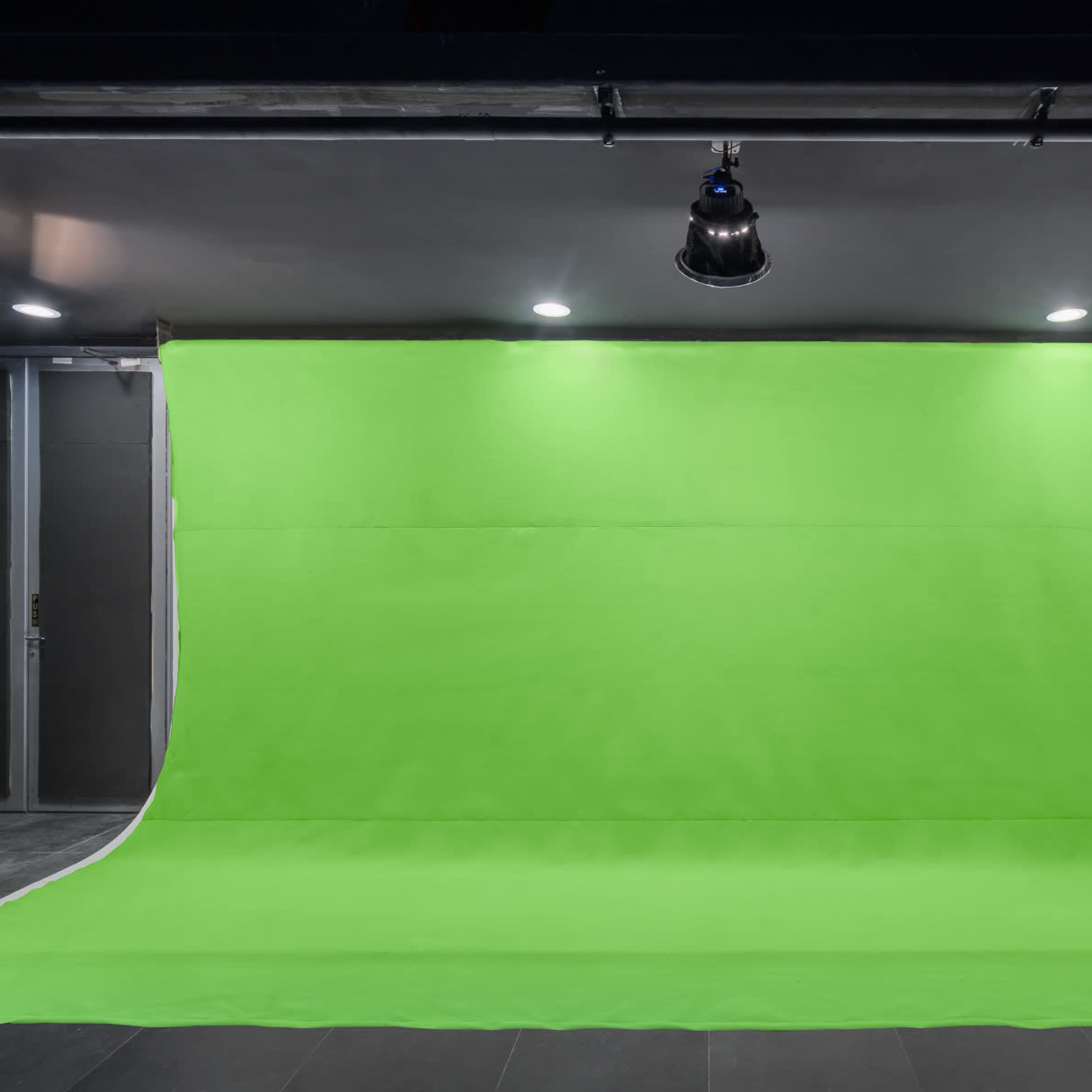 A photography studio with a large green backdrop and overhead lighting.