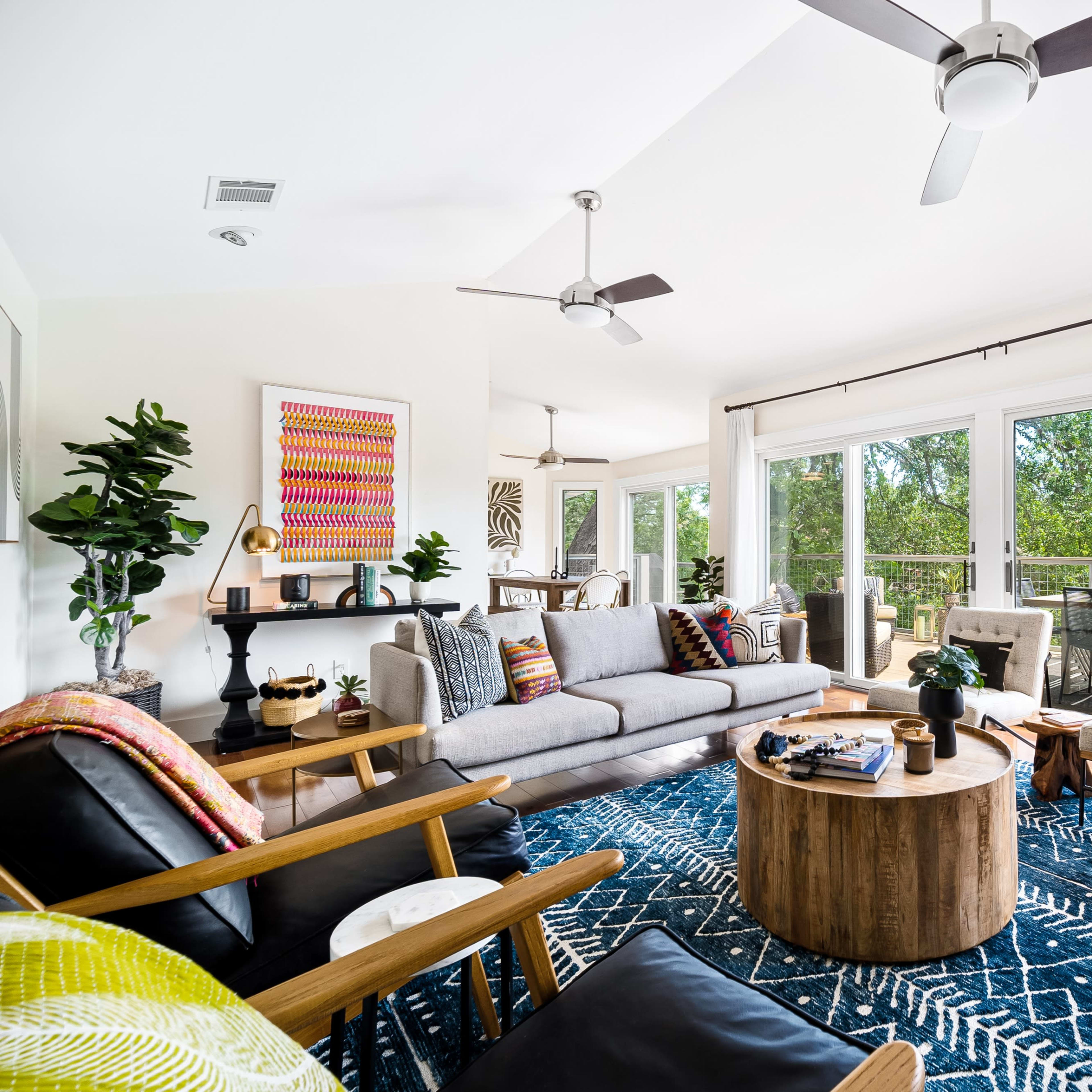 A bright living room with a large sectional sofa, a wooden coffee table, and floor-to-ceiling windows overlooking a scenic view.
