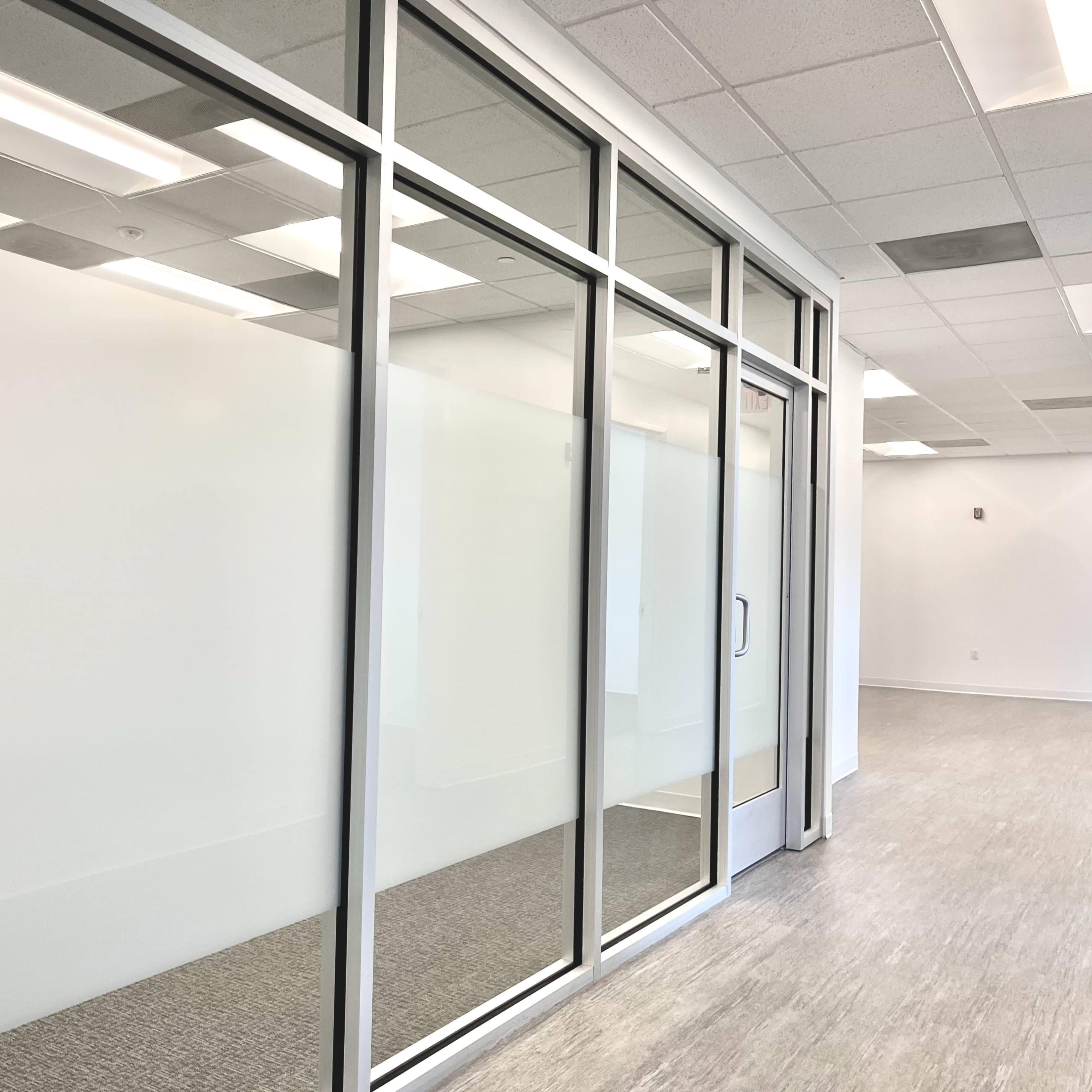 A modern office space featuring large glass panels with a frosted section and a doorway.