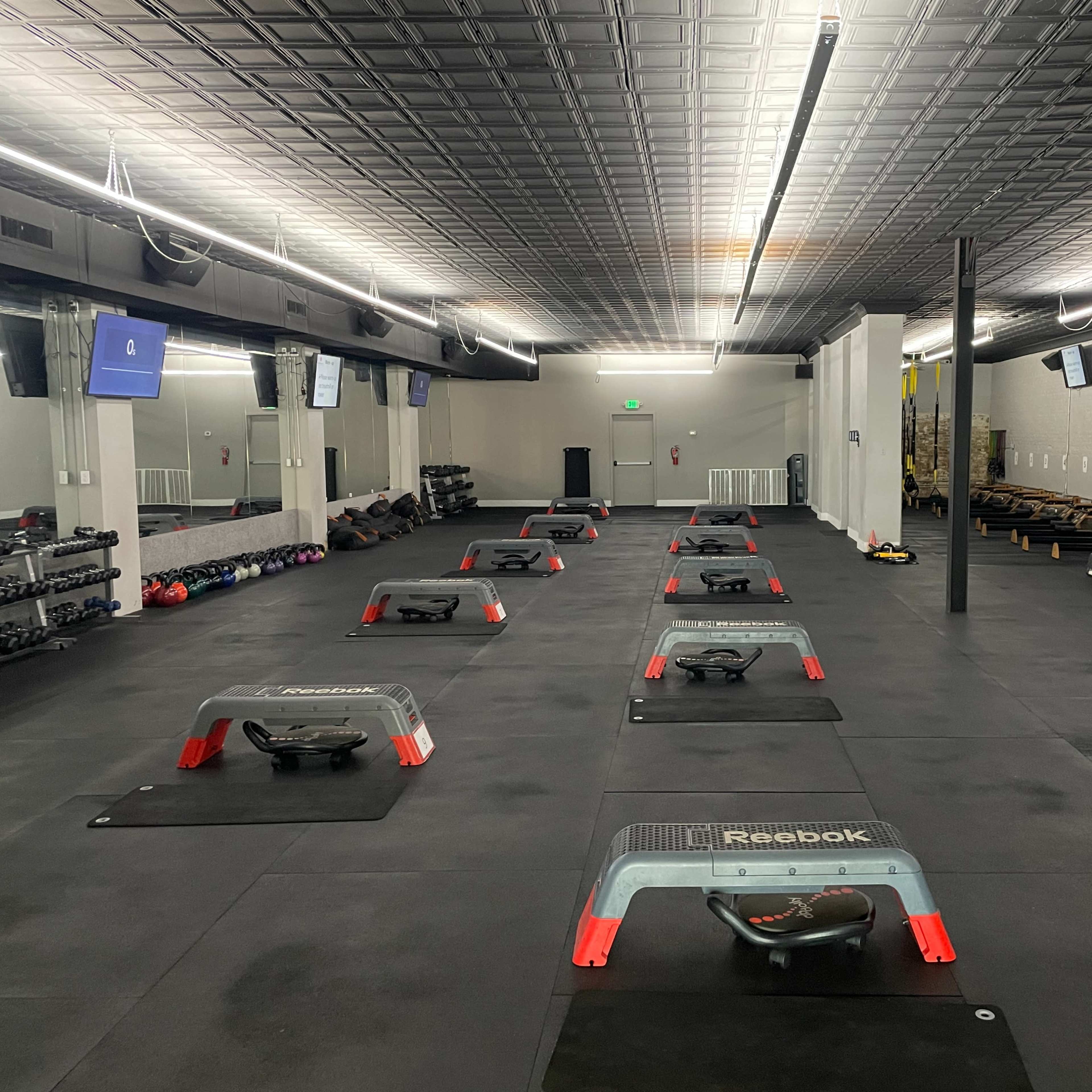 An empty gym with multiple exercise stations set up on a black rubber floor, along with various gym equipment including dumbbells and treadmills.