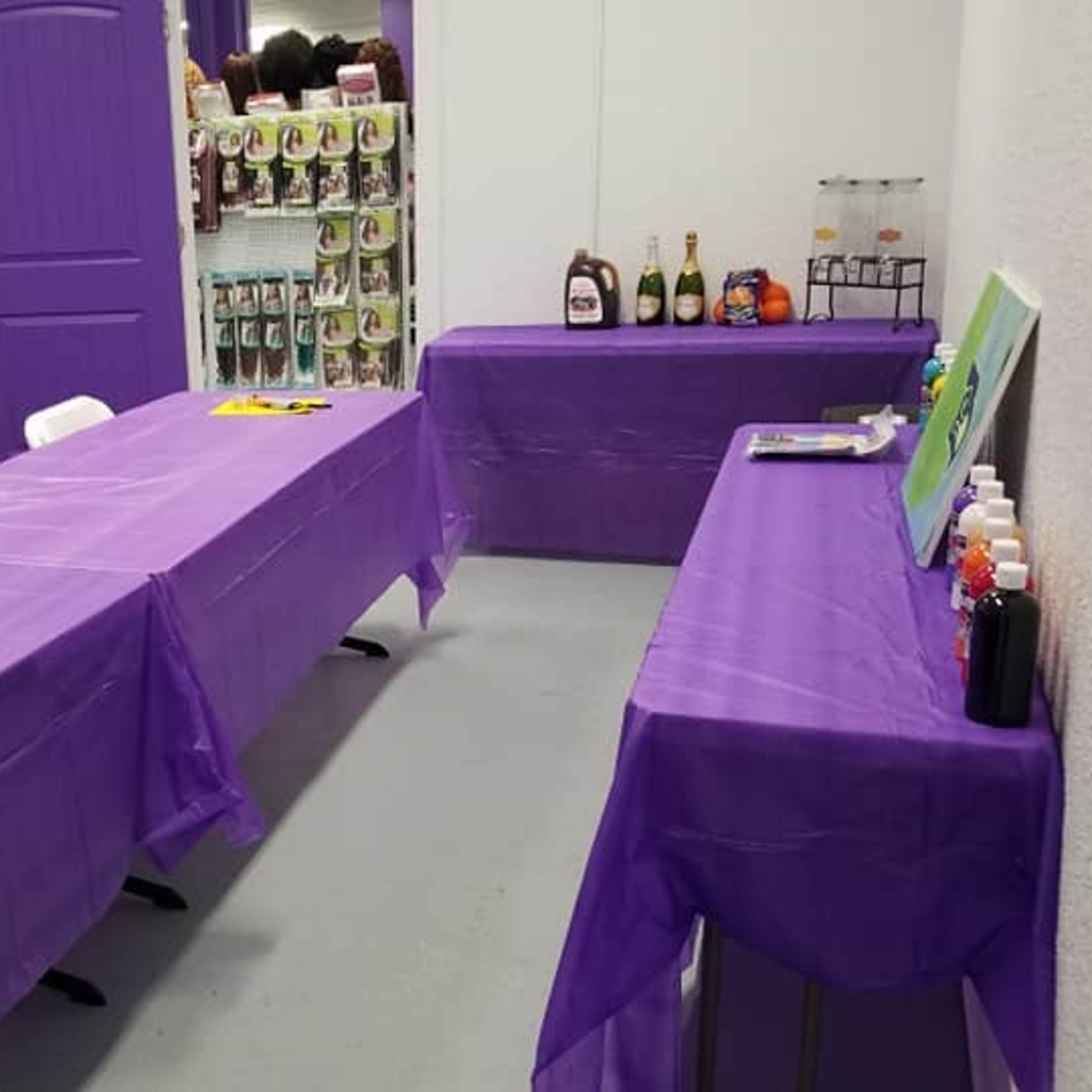 A room with several purple-covered tables and a small bar area, set up for an event or gathering.