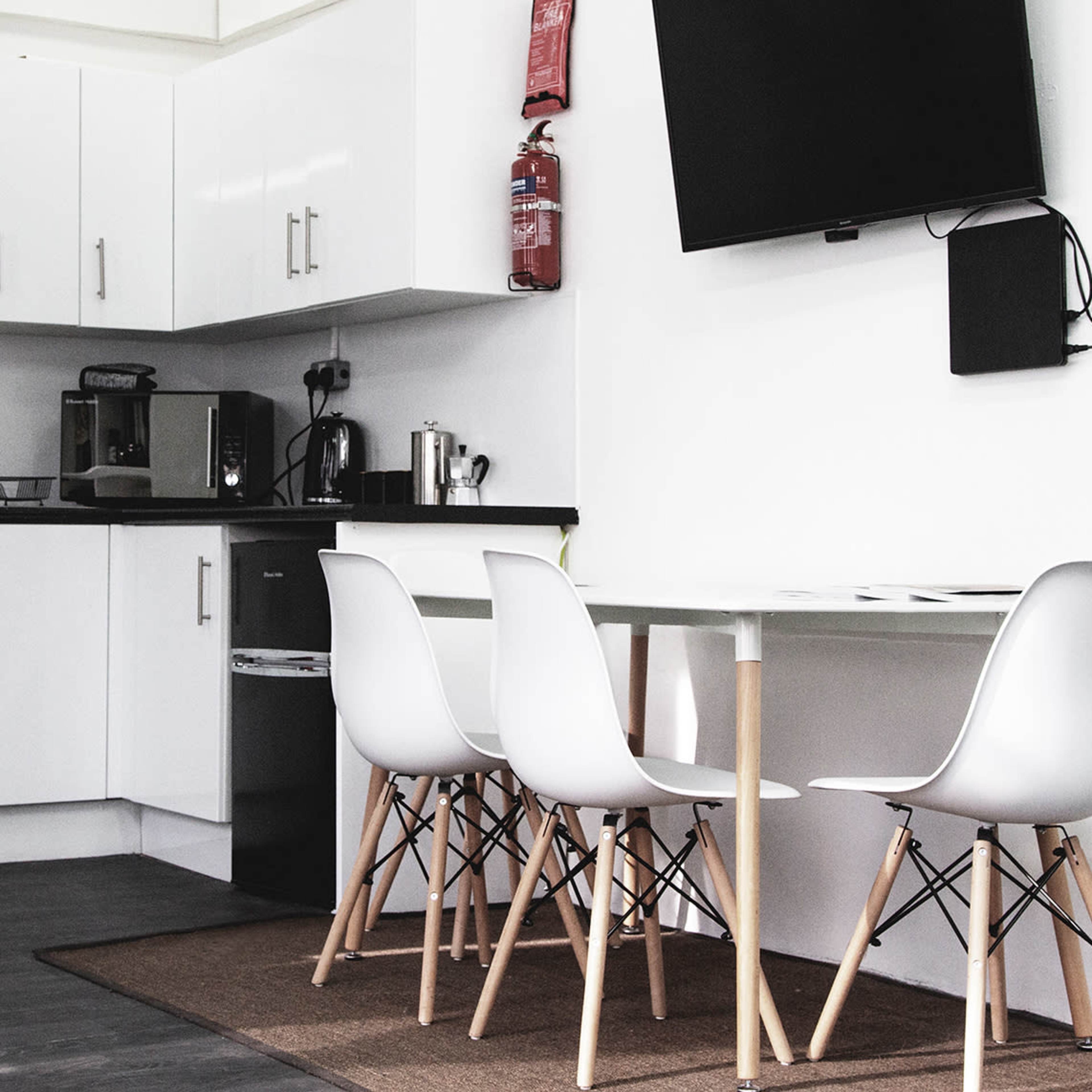 A modern kitchen area features white cabinets, stainless steel appliances, and a dining table with four white chairs.