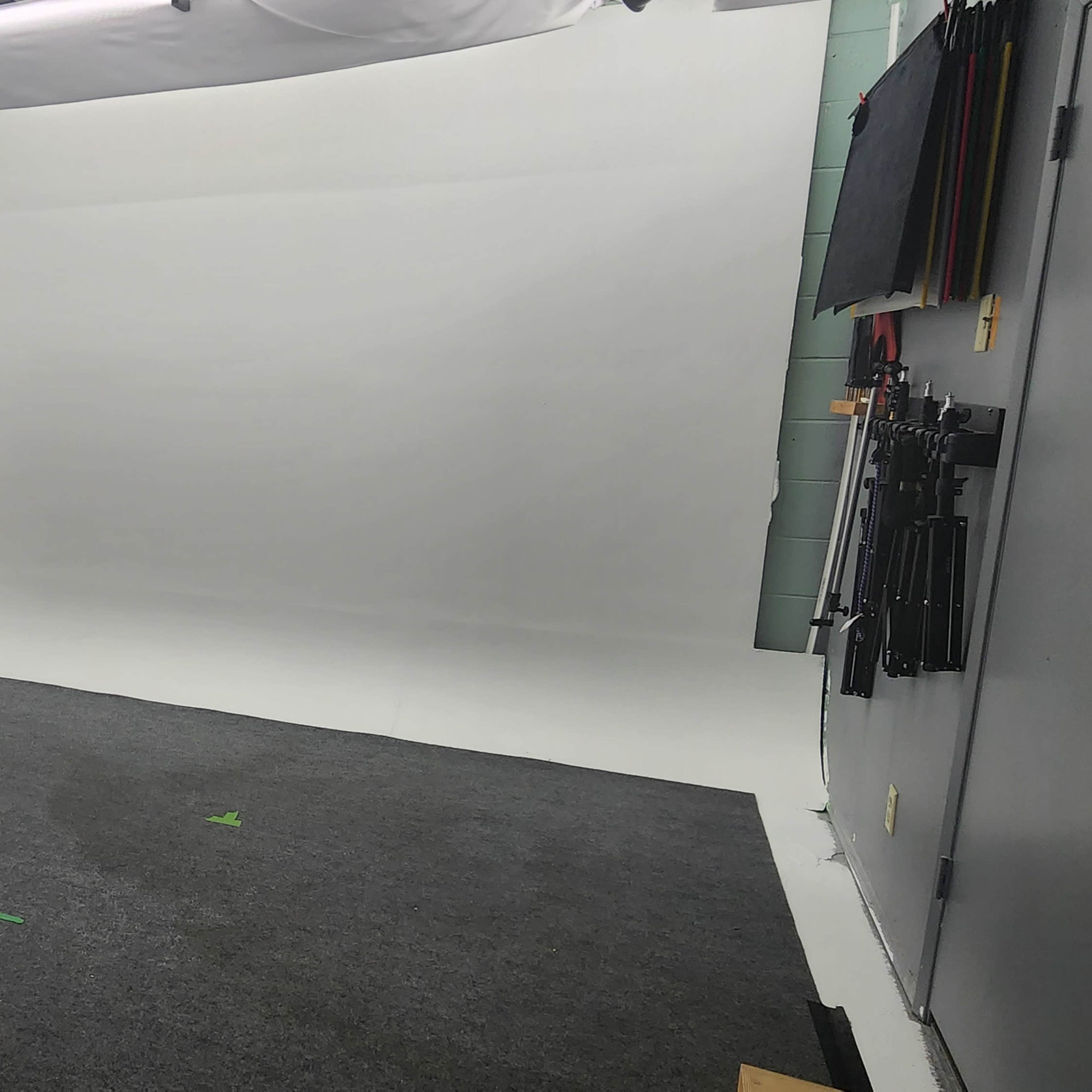An empty studio space with a gray carpet and a seamless white backdrop.