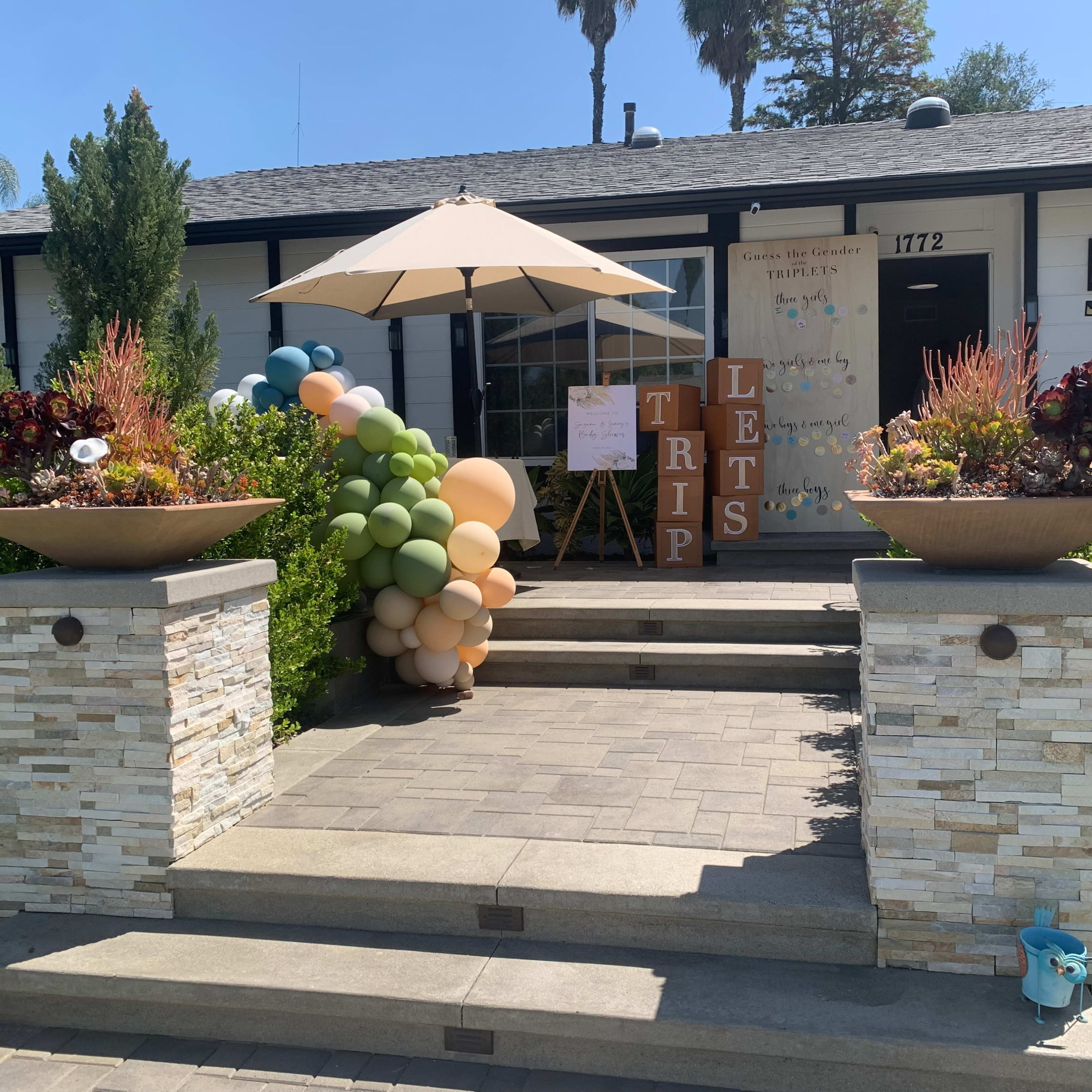 A residential entrance features a well-maintained front yard with decorative planters, a balloon arch, and a sign promoting a trip.