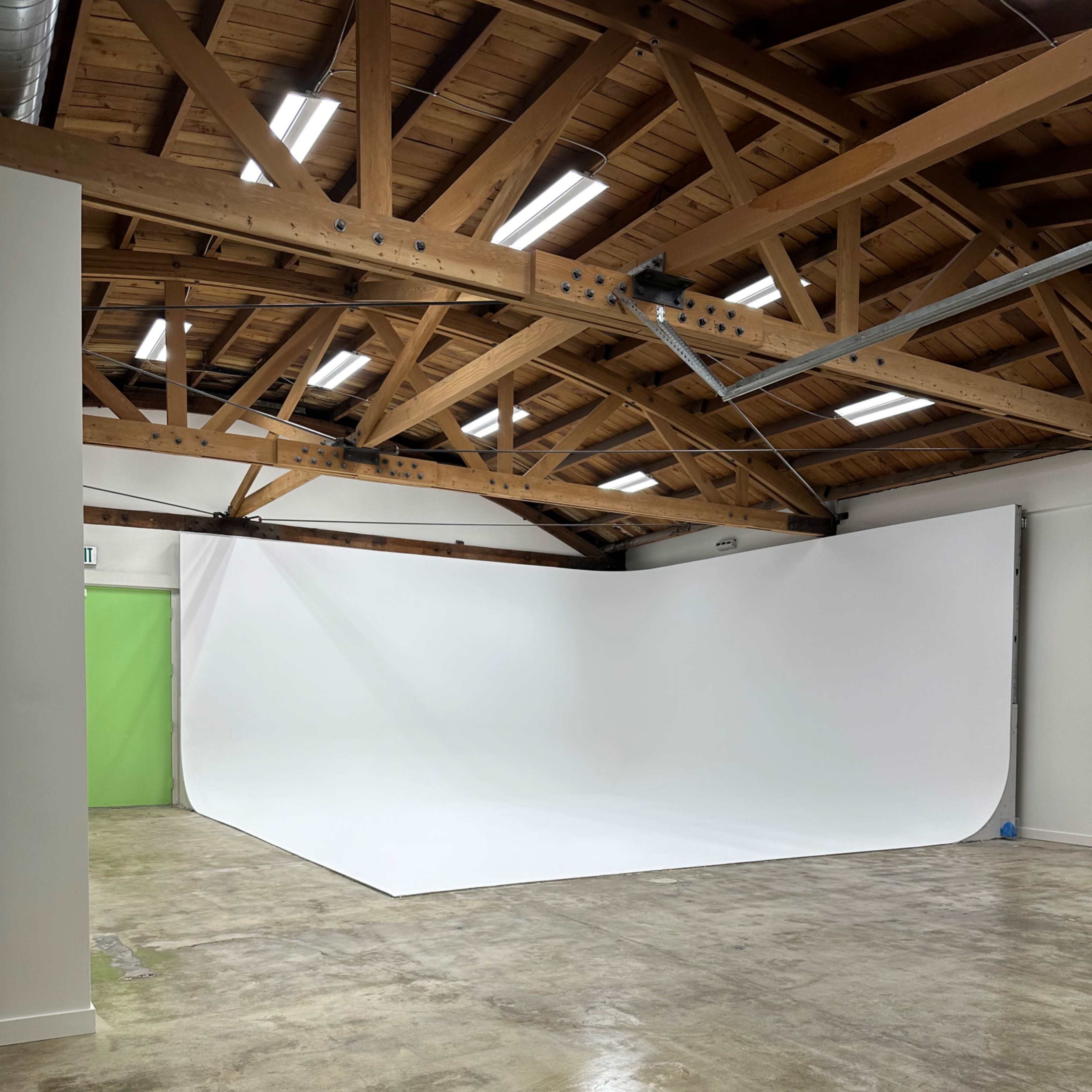 A spacious photo studio with a white backdrop and exposed wooden beams in the ceiling.