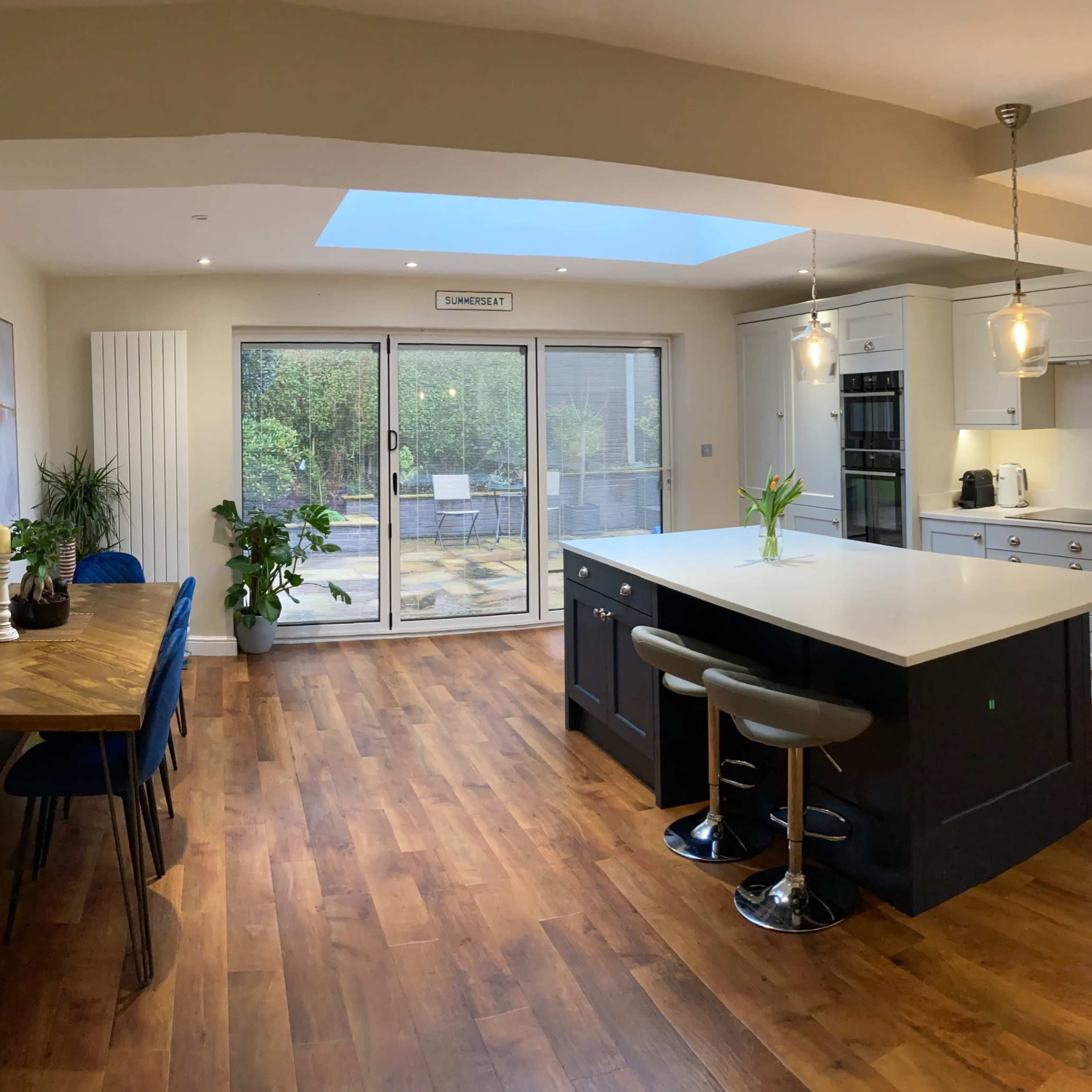 A modern kitchen features an island with seating, wooden flooring, and large sliding doors leading to an outdoor patio.