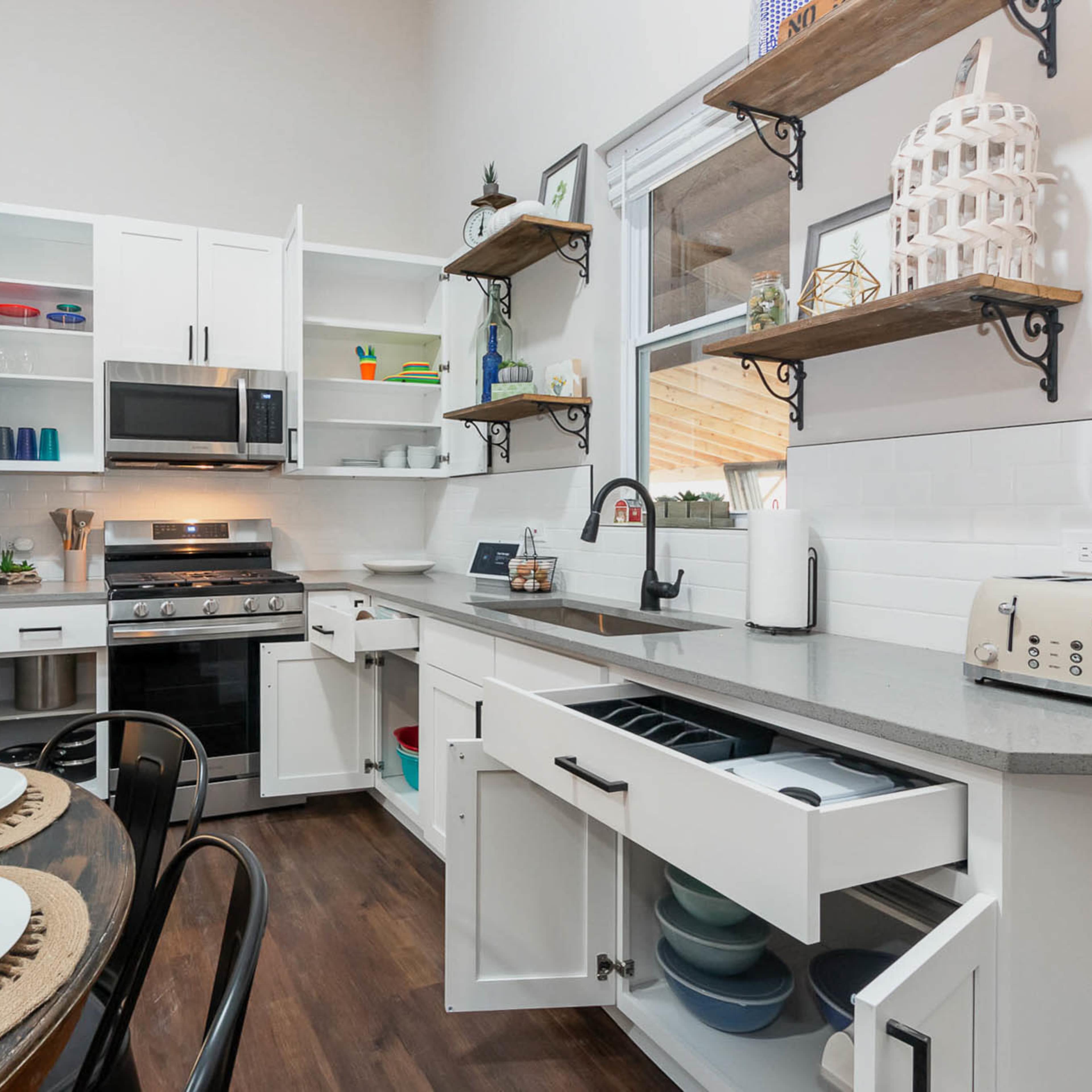 A modern kitchen features white cabinets, stainless steel appliances, and open shelving with various dishes and utensils.