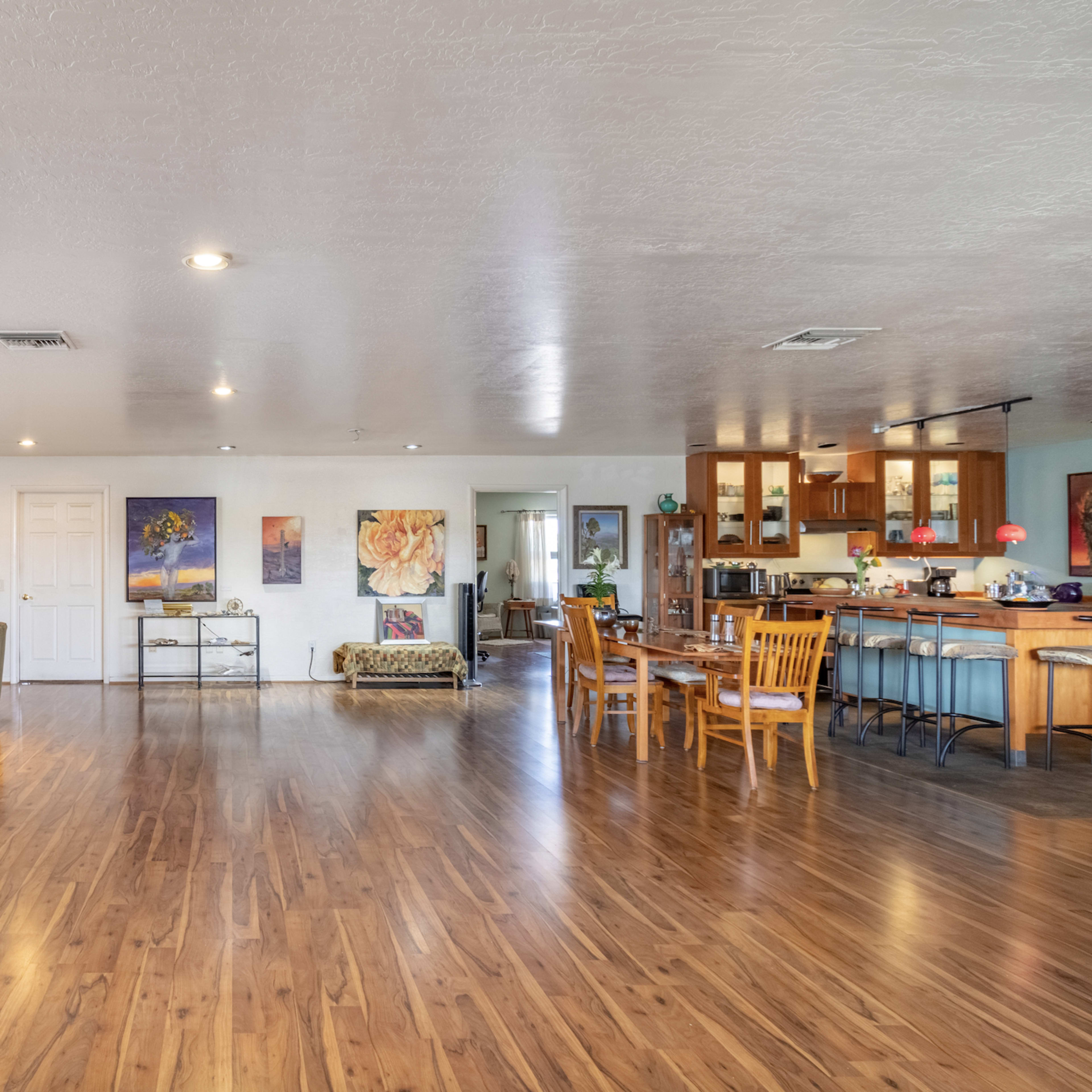 A spacious living area features a green sofa, wooden dining set, and a kitchen with wooden cabinets, all illuminated by overhead lights.