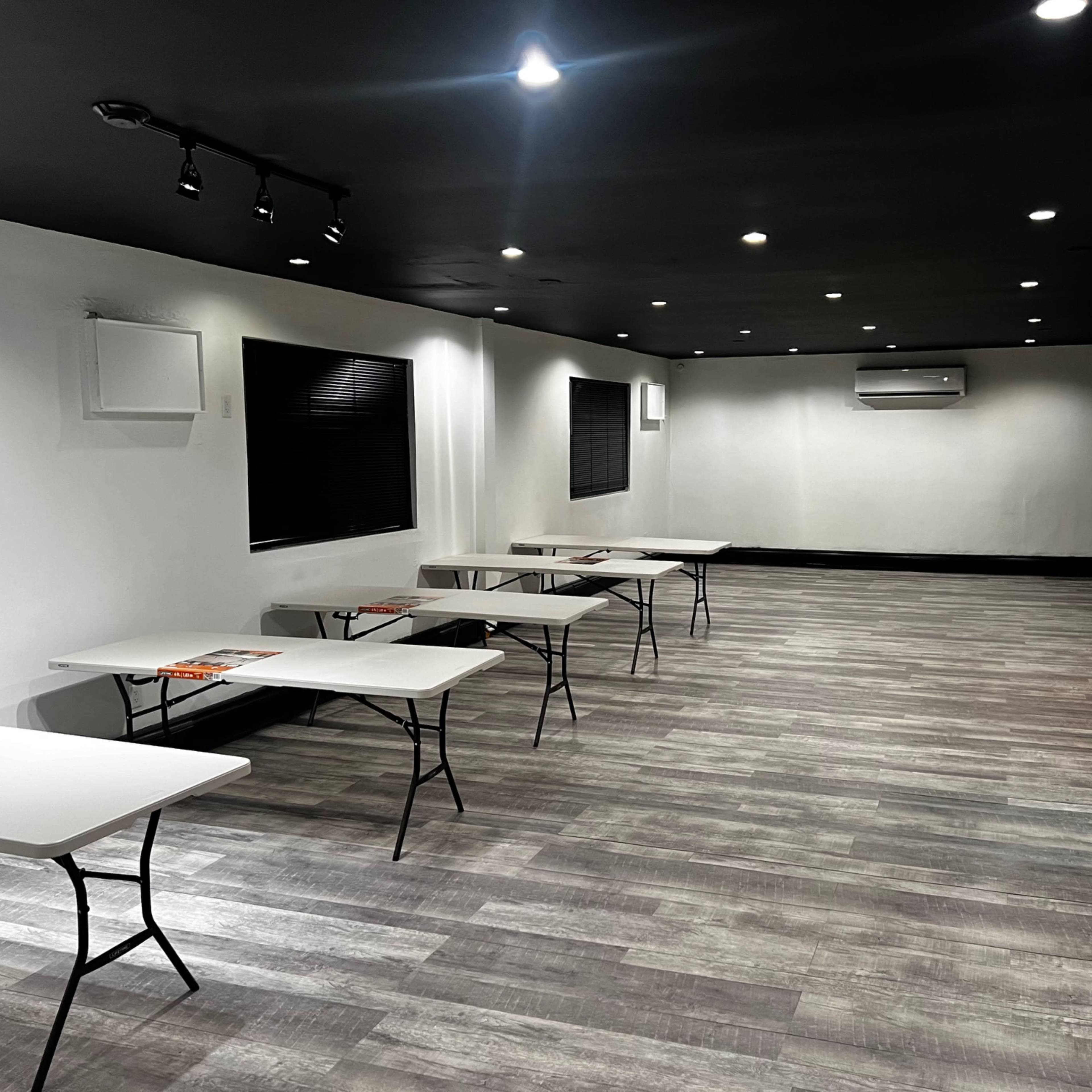 An empty room with several tables arranged in a spacious layout, featuring dark walls and modern lighting.