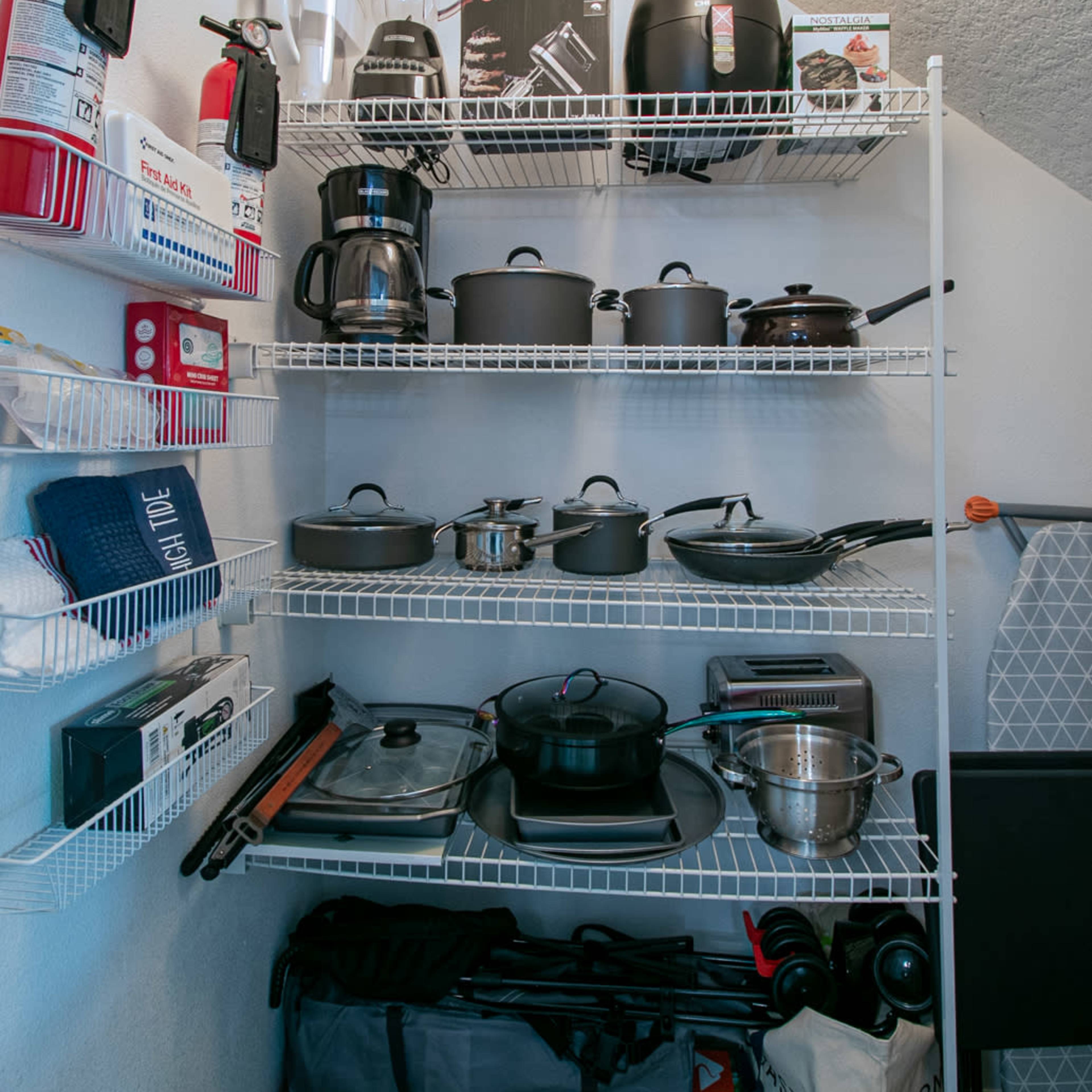 A neatly organized shelving unit displays various kitchen appliances, cookware, and utensils, alongside fire extinguishers and additional storage items.